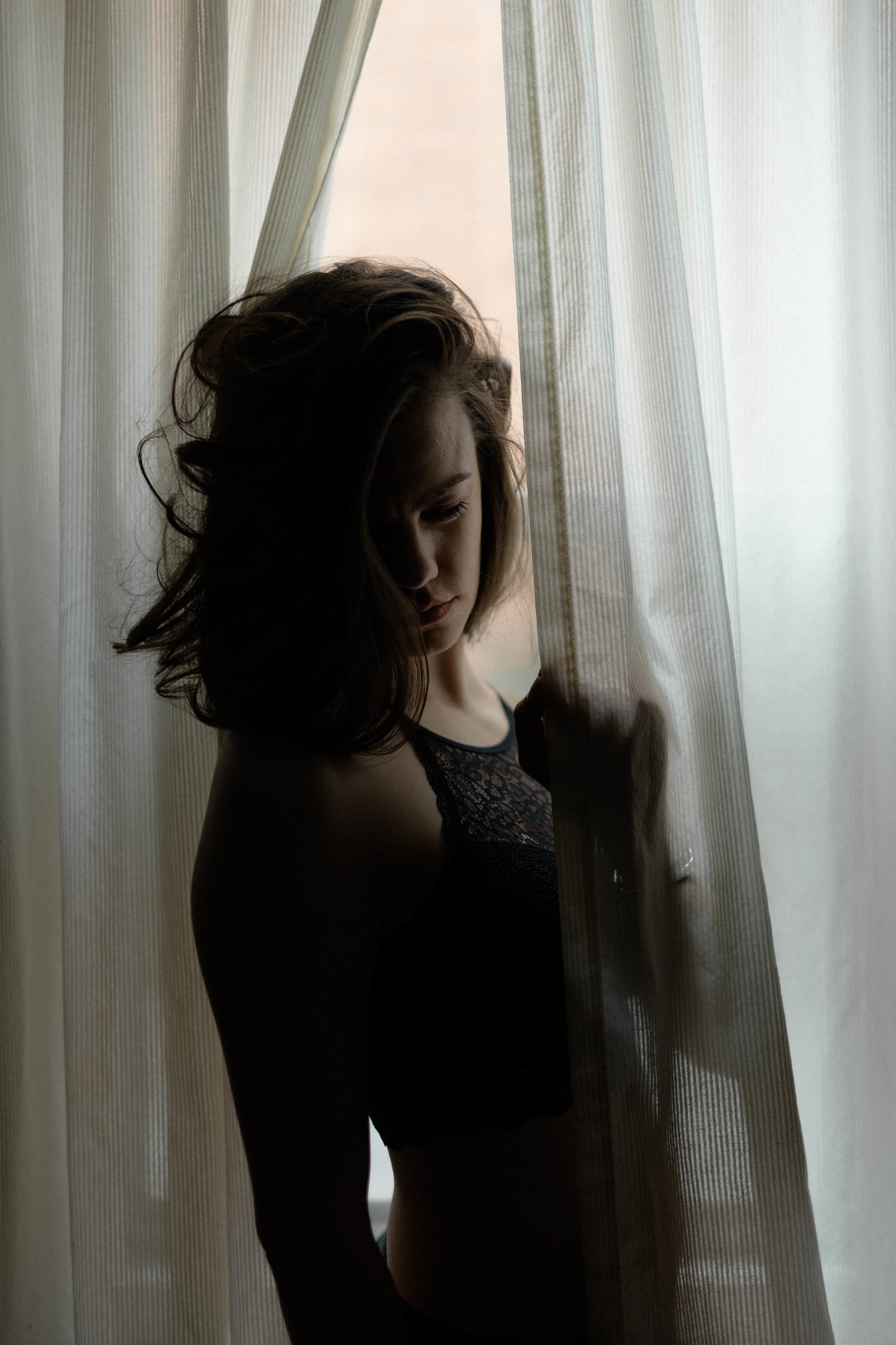  a portrait of emma grimsley in a victorian airbnb in dayton, ohio. photograph by sarah rose walk of sarah rose photography. the portrait has emma placed between two slightly sheer curtains, and she is looking down with her hair gently covering her f