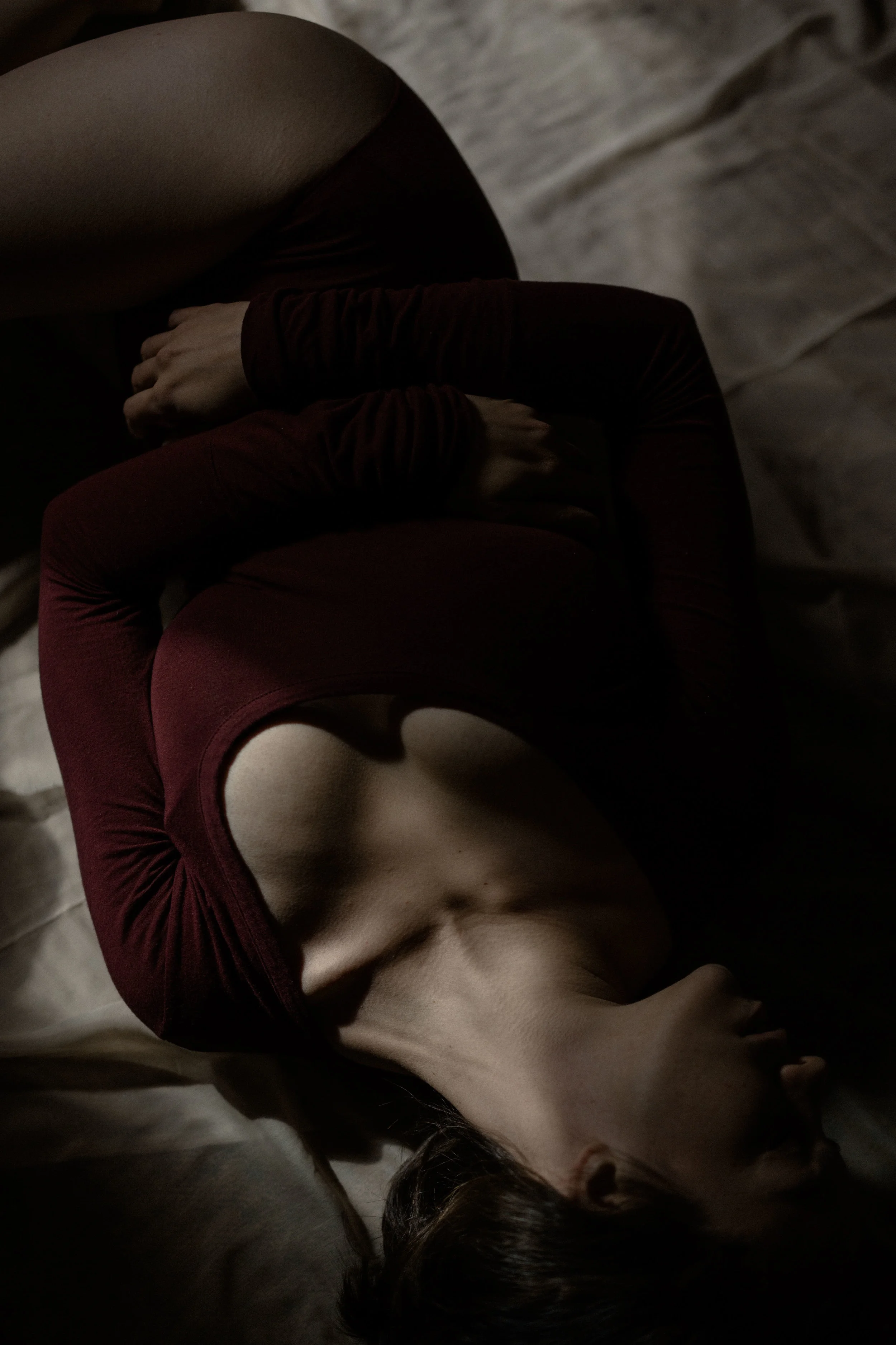 a portrait of emma grimsley in a victorian airbnb in dayton, ohio. photograph by sarah rose walk of sarah rose photography. emma is laying in a sun spot on the ground, and she is looking to the side. emma is wearing a long sleeve burgundy red bodysuit.