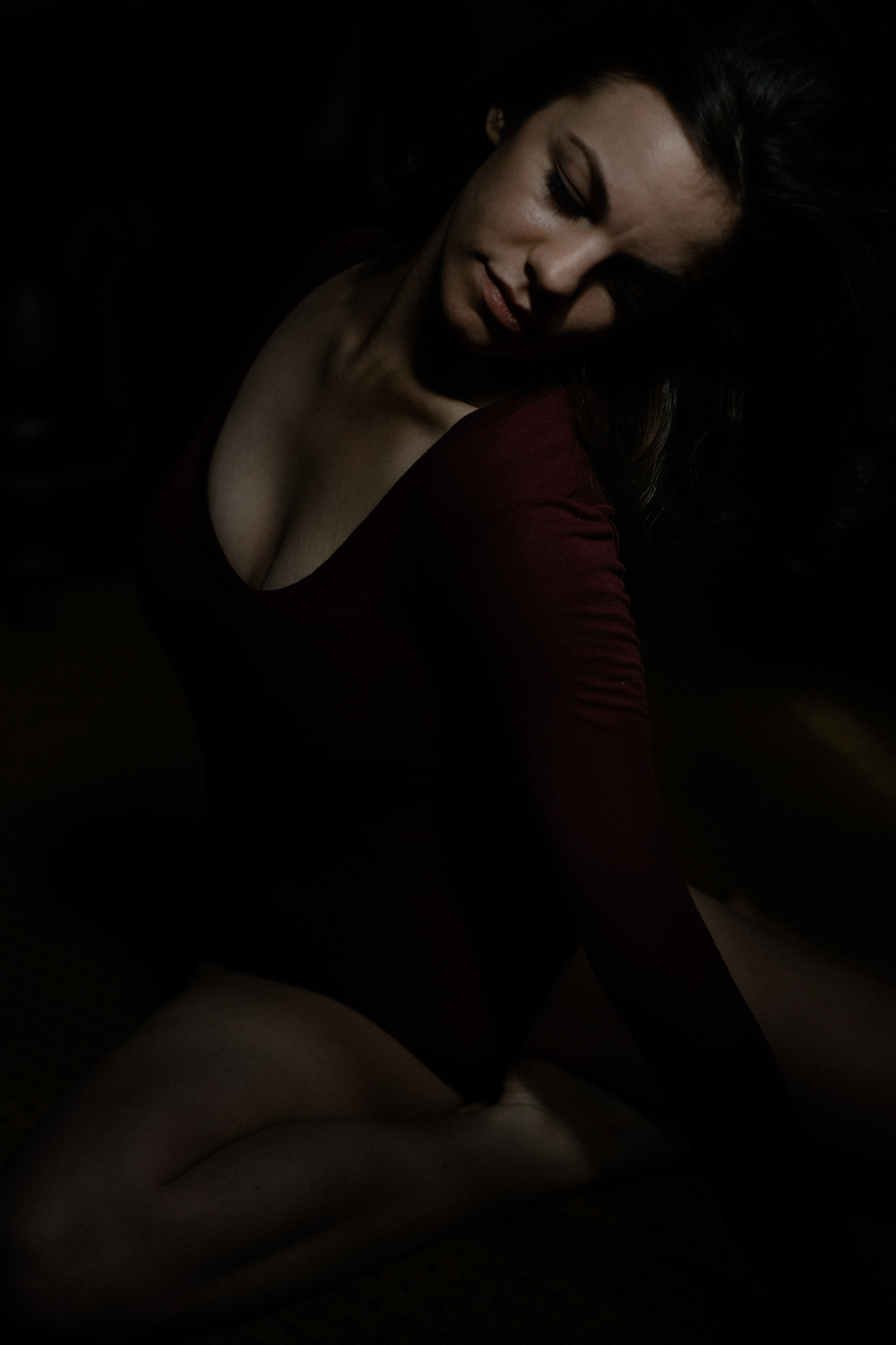  a portrait of emma grimsley in a victorian airbnb in dayton, ohio. photograph by sarah rose walk of sarah rose photography. emma is sitting on the ground, and she is looking to the side, twisting her body. emma is wearing a long sleeve burgundy red 