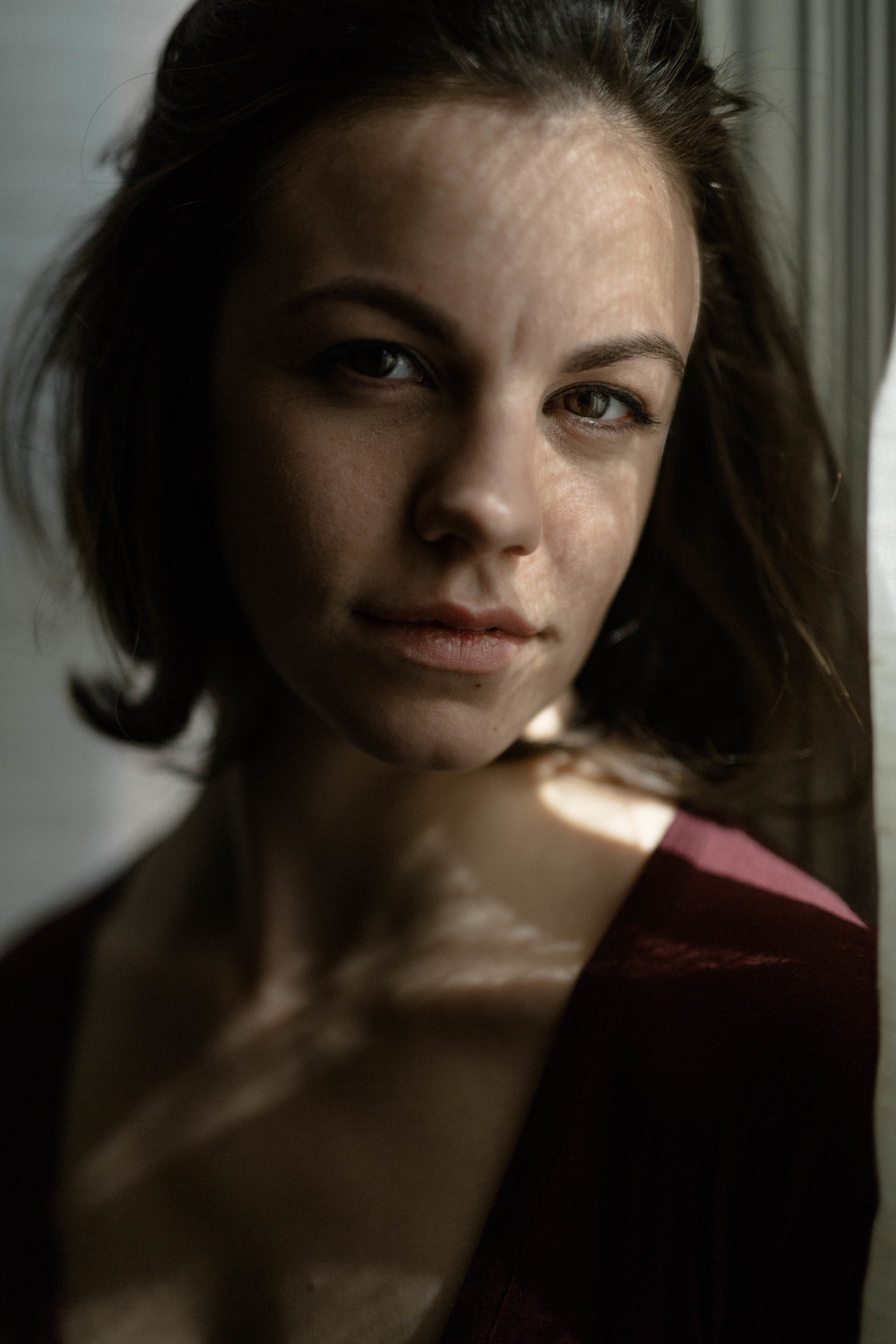  a portrait of emma grimsley in a victorian airbnb in dayton, ohio. photograph by sarah rose walk of sarah rose photography. emma is leaning against a window and the photograph is of her face: a classic portrait. emma is wearing a long sleeve burgund