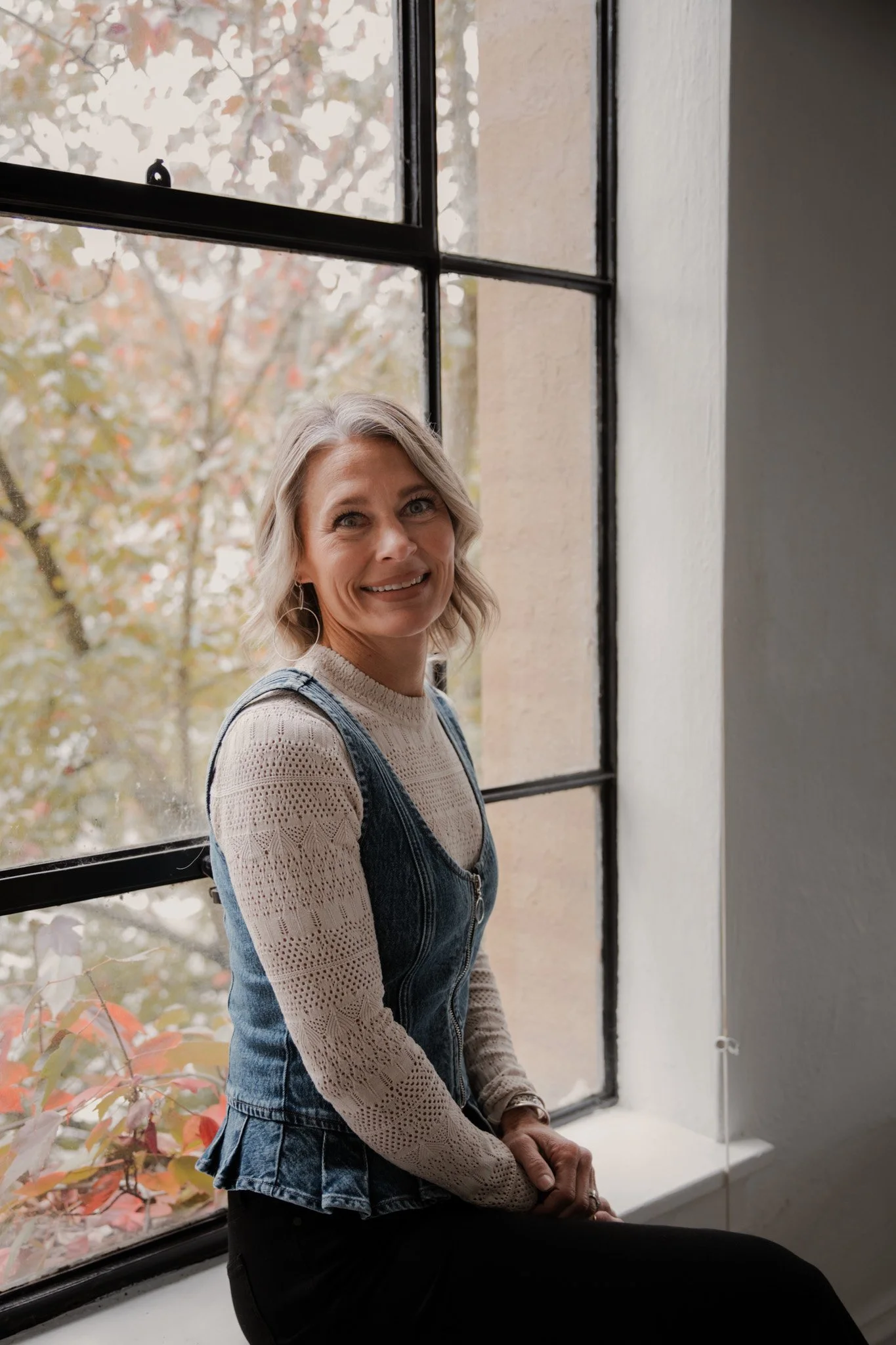 Annie Weygandt, hair stylist at Modèle Salon in Oregon City, smiling in a denim vest by a window