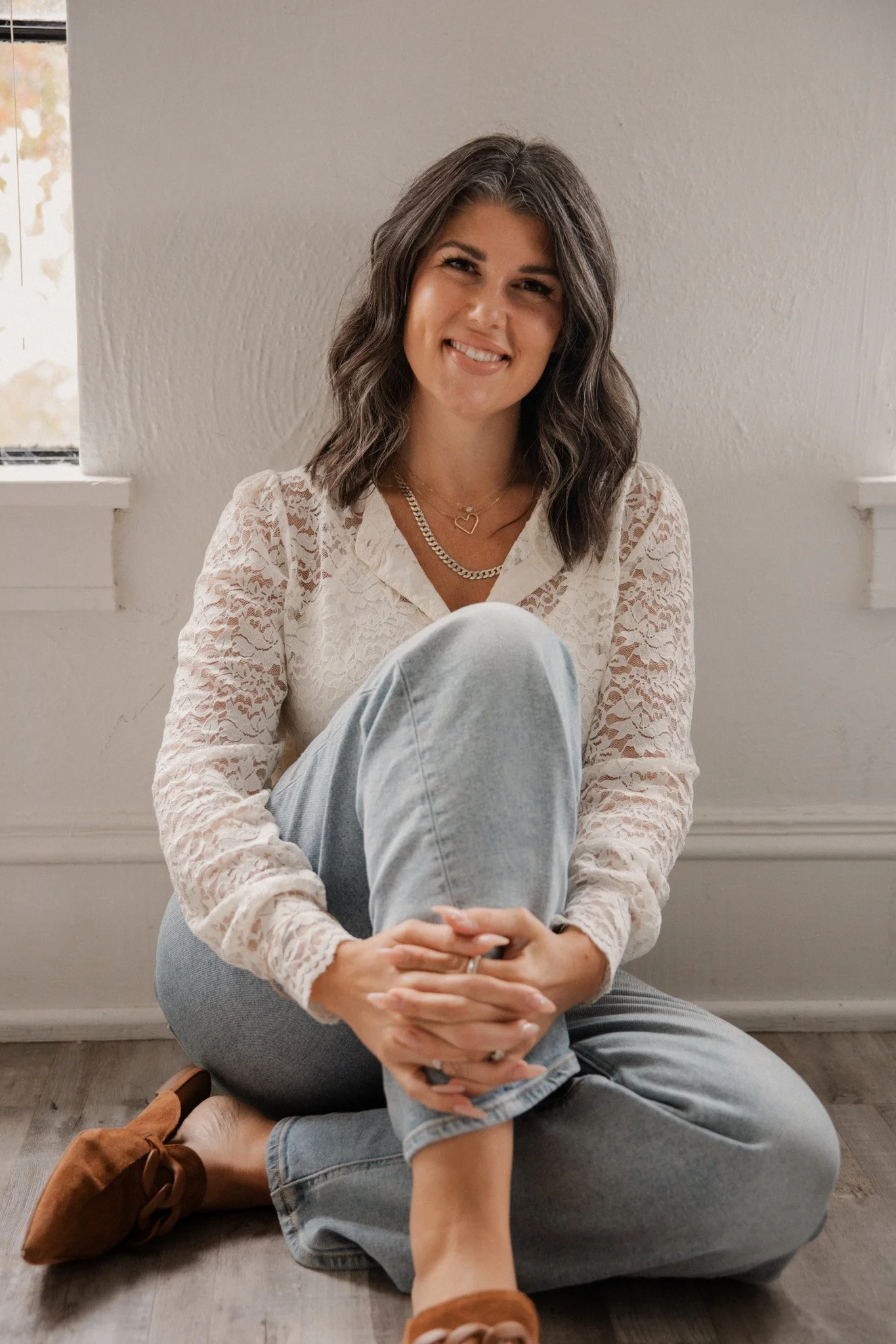 Michelle Ketchum, hair stylist at Modèle Salon in Oregon City, sitting and smiling in a white lace top