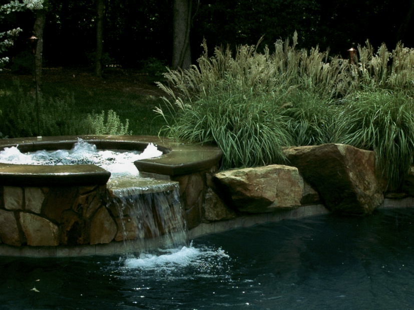 Raised spa wall with fieldstone veneer and 6x6 waterline tile. Boulders set on pool edge and Black Pebble Finish.