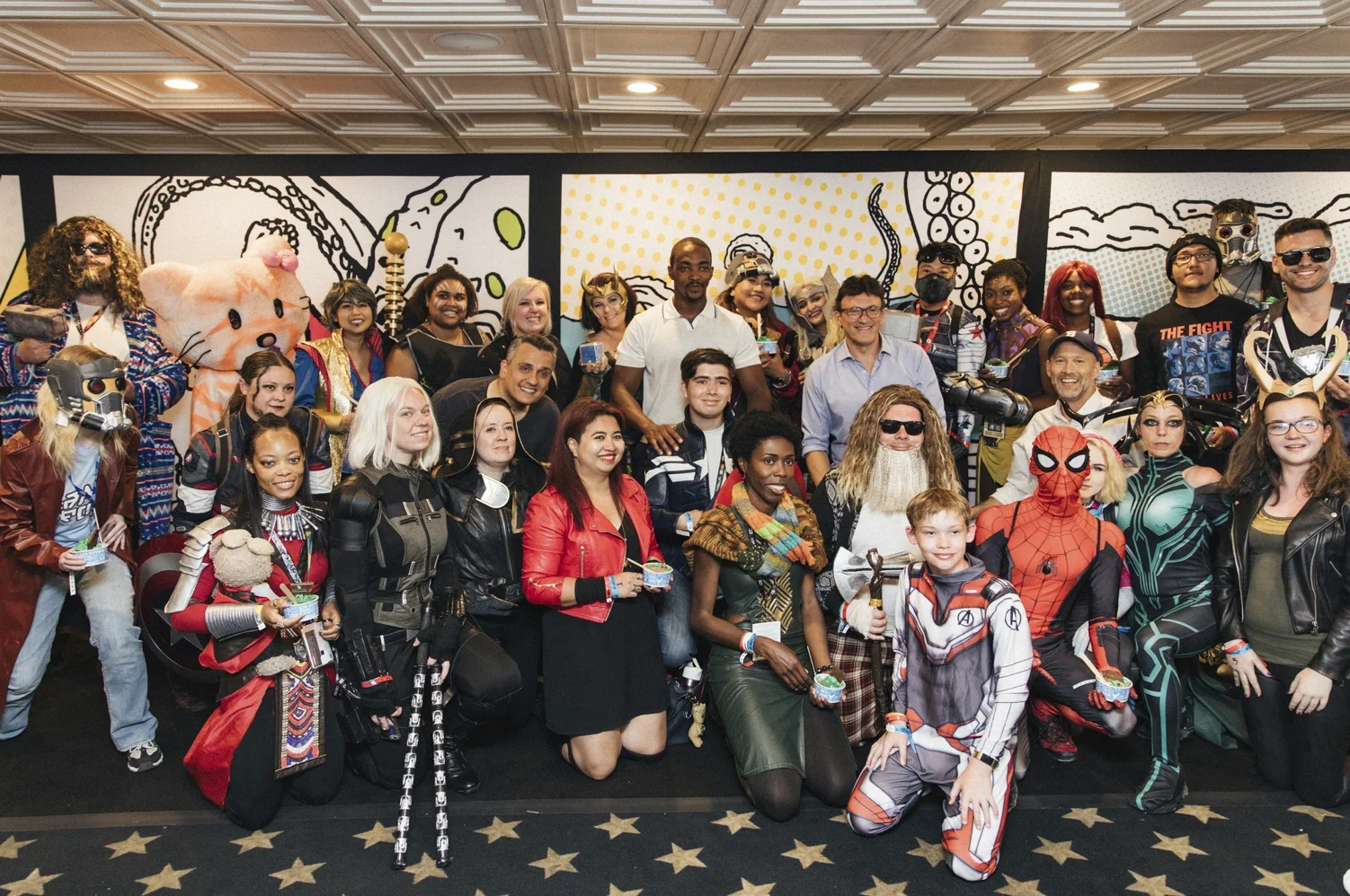 The Russo Brothers & Anthony Mackie posing with fans in front of IMBd Boat mural