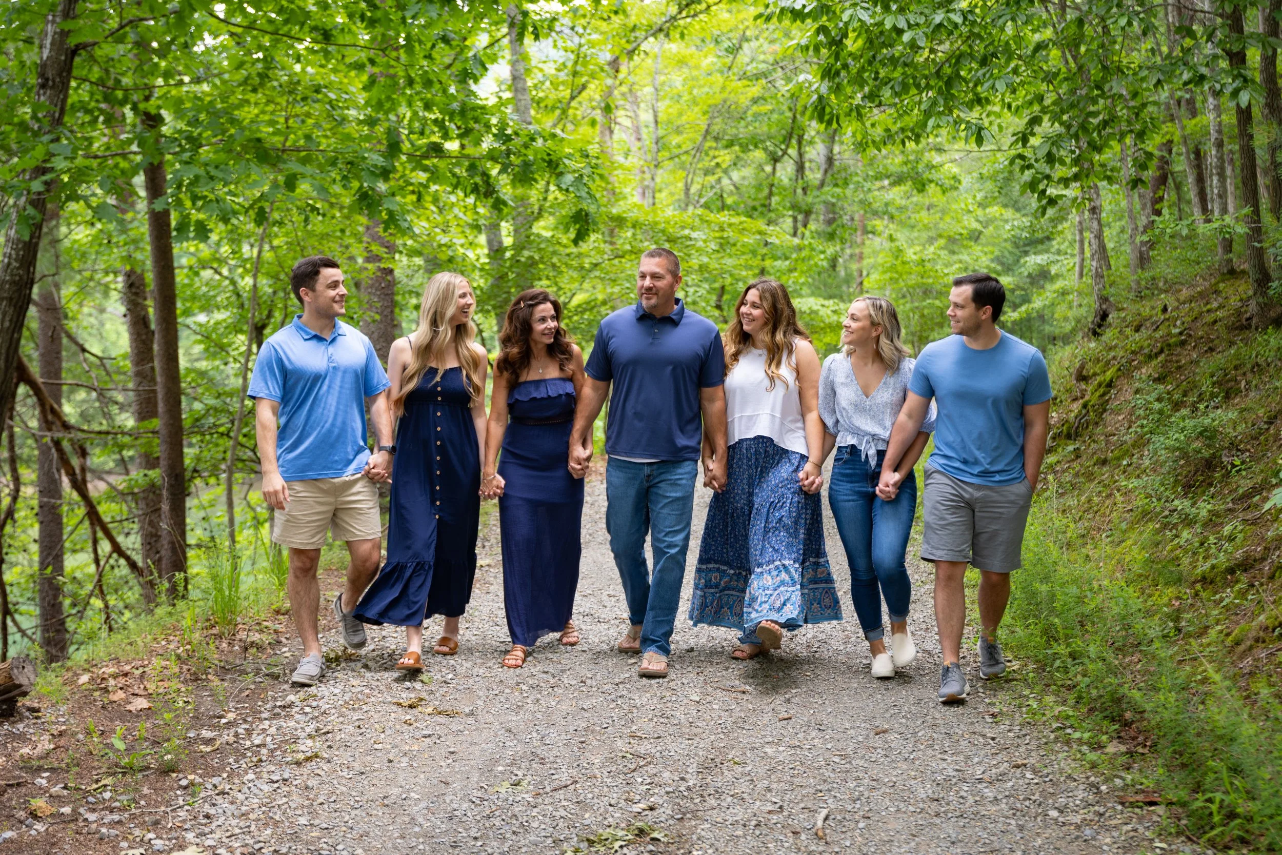 Group of six young adults holding hands and walking in a lush green forest.