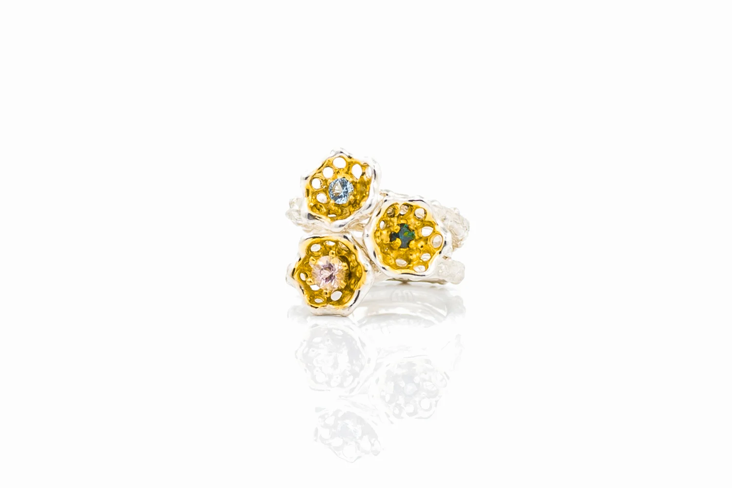 Three stackable silver cusp rings hold aquamarine, Australian sapphire and morganite. Each stone is protected by curved and organic golden surfaces.