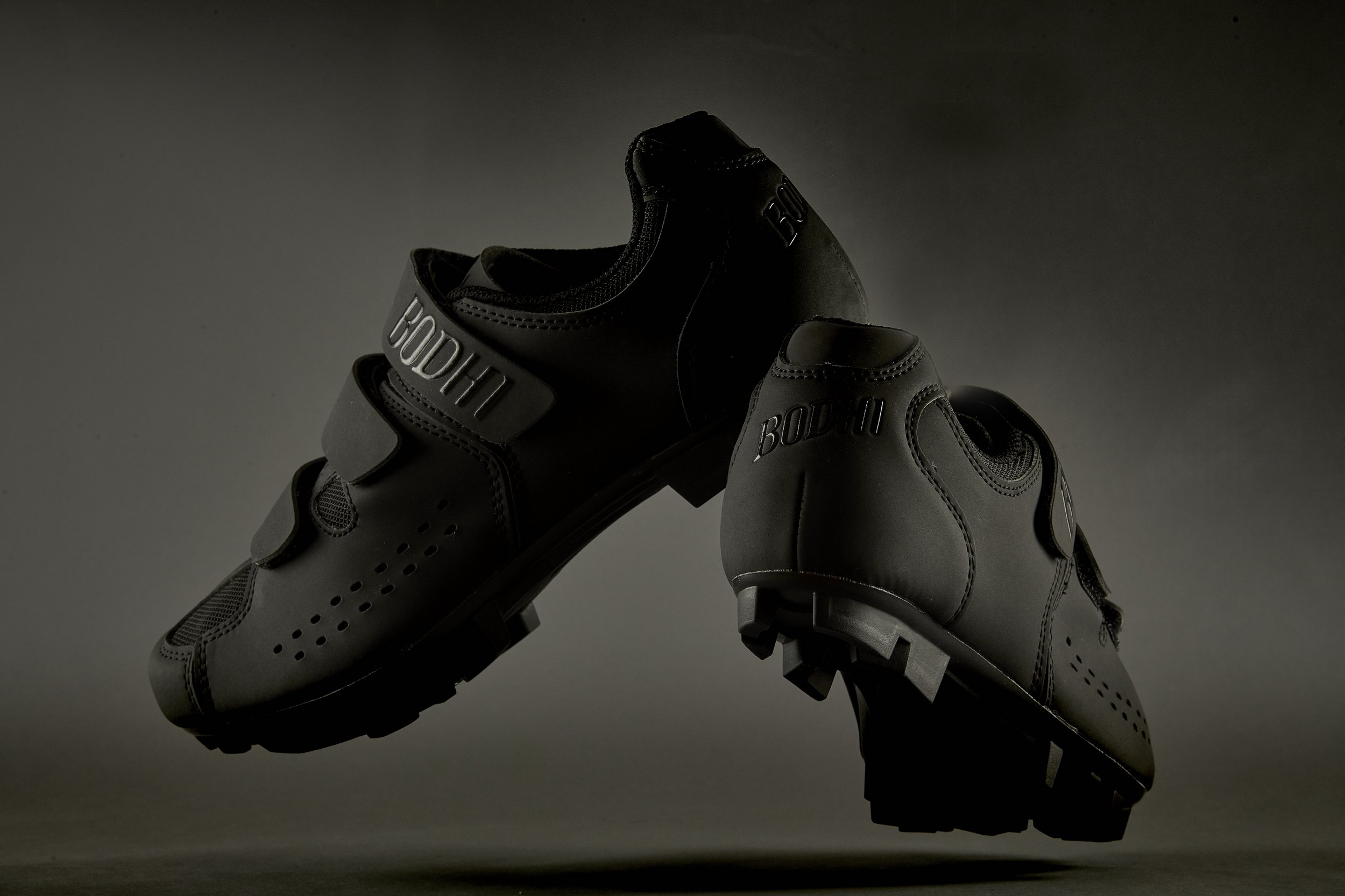 A pair of black athletic shoes with the word 'BODHI' on the side, set against a dark gray background.