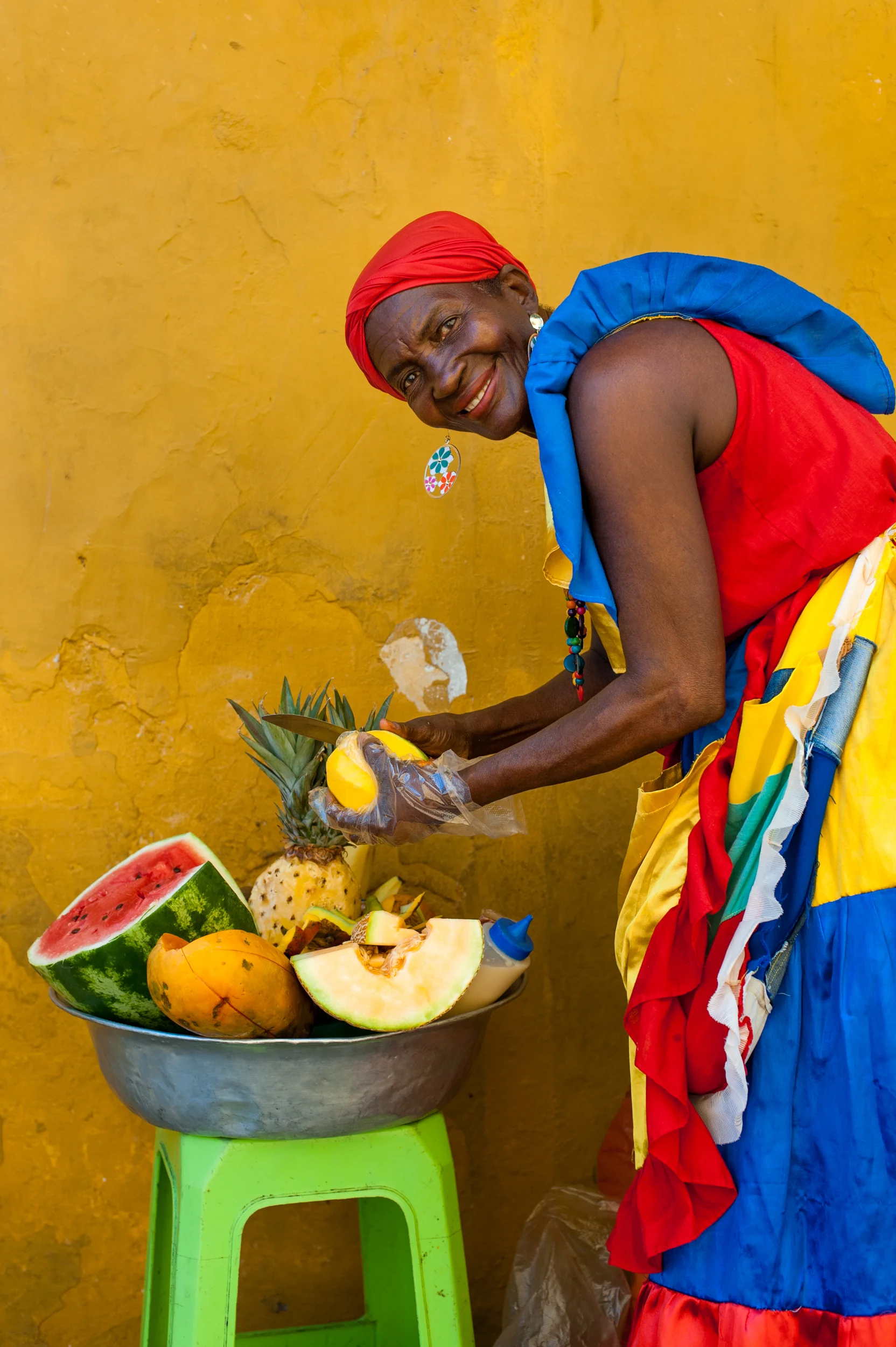 Colombia Woman dressed in traditional clothes cutting and selling fruit in the colorful old town of Cartagena. Colombians are blessed with a fertile country and an eye-popping array of tropical fruit.