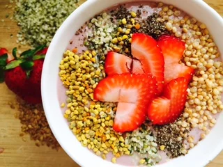 Smoothie bowl topped with strawberries, bee pollen, hemp seeds, chia seeds, and quinoa puffs 