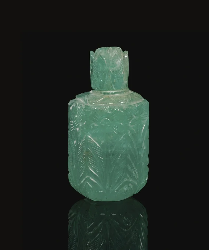 A Mughal carved emerald flask with stopper, India, circa 18th century. The body of faceted hexagonal form, cut and carved on each face with a floral stem, the stopper carved with eight stylised leaves and a star design to the top. Sotheby's