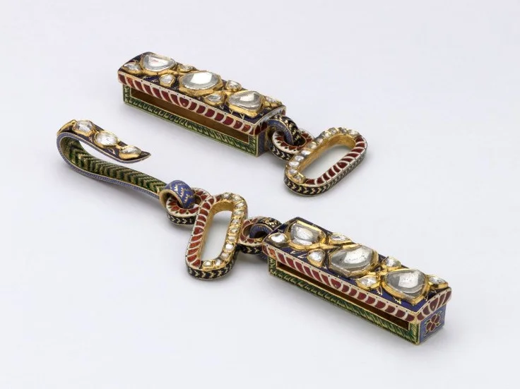 Mughal gold and enamel belt buckle in two pieces with inlaid diamonds. Enamel decoration on reverse of tiger attacking a boar. b. Rectangular element with small round ring through which oblong ring fits. Hook is attached to this. Enamel tiger attacking a deer in foliage on reverse of rectangular element. British Museum