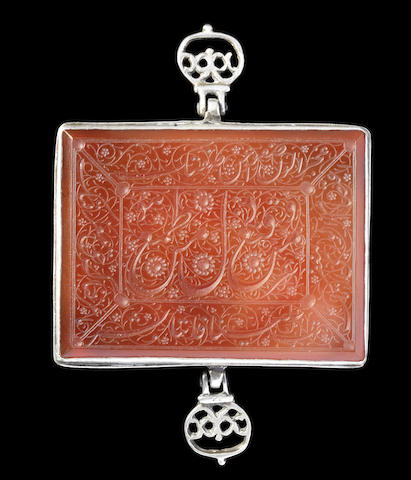 A Qajar silver-mounted inscribed carnelian Armband (bazuband), Persia, 19th Century. Rectangular, engraved with a central cartouche containing inscriptions on a ground of floral interlace, surrounded by four panels containing inscriptions on a ground of scrolling floral vines, the silver mount with two hinged suspension loops decorated in openwork with foliate motifs 8 x 6 cm. Image: Bonhams