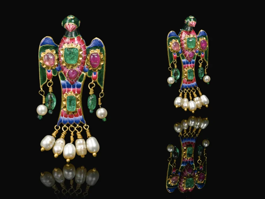 A Qajar gold, enamelled and gem-set eagle-form brooch, Persia, 19th century with wings outstretched, decorated throughout in polychrome enamels, set with emeralds and rubies, with pendant pearls suspended from the wings and tail by gold wire elements, fitted with a pin at the back. 7cm. Image: Sotheby's