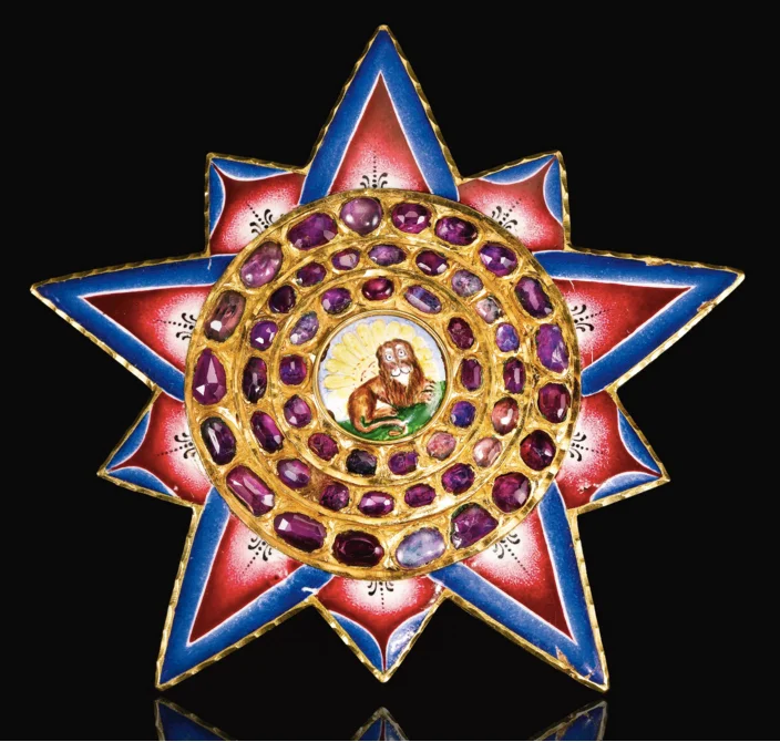 A gold, enamelled and jewelled insignia of the Qajar order of the Lion and Sun, Persia, early 19th century of stellar form with stepped gold frame set with rubies featuring an enamelled medallion with recumbent lion in front of a rising sun, the rays with gradated pink and blue bands, hinged pin for attaching to reverse. 9cm. Image: Sotheby's