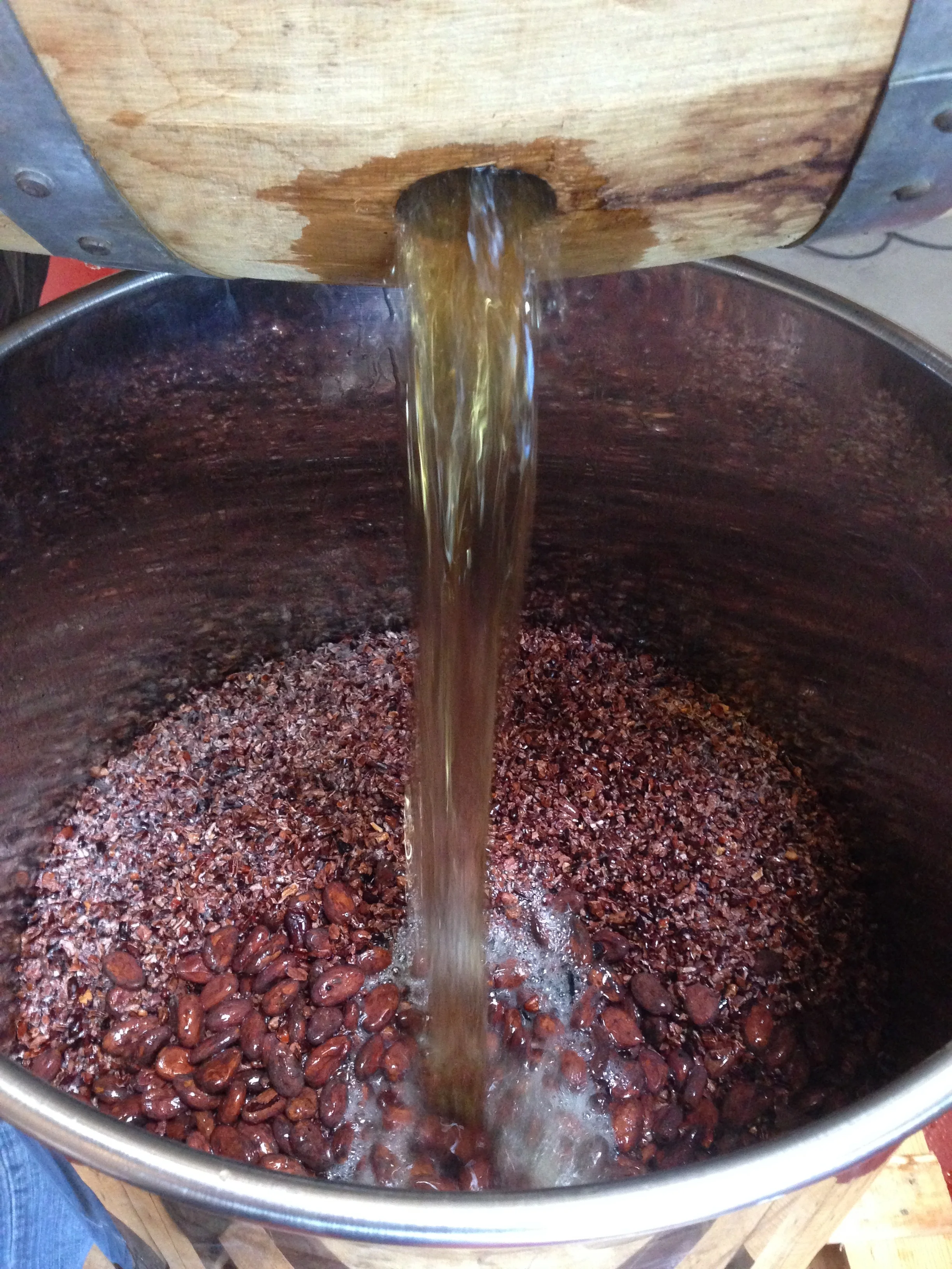 The distiller adding barrel-aged California rye whiskey to whole cacao and cacao nibs.
