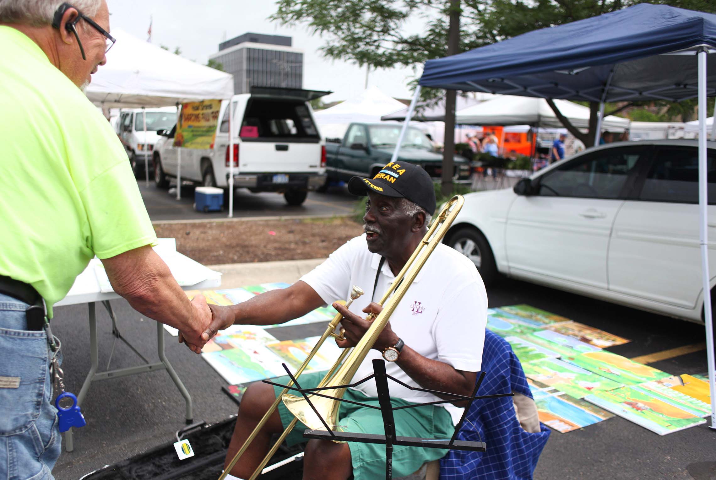  Willie Dixon, right, of Kankakee, shakes a viewers hand Saturday during the Kankakee Farmers Market in downtown Kankakee. Dixon sells his original paintings and plays the trombone for passers by. 