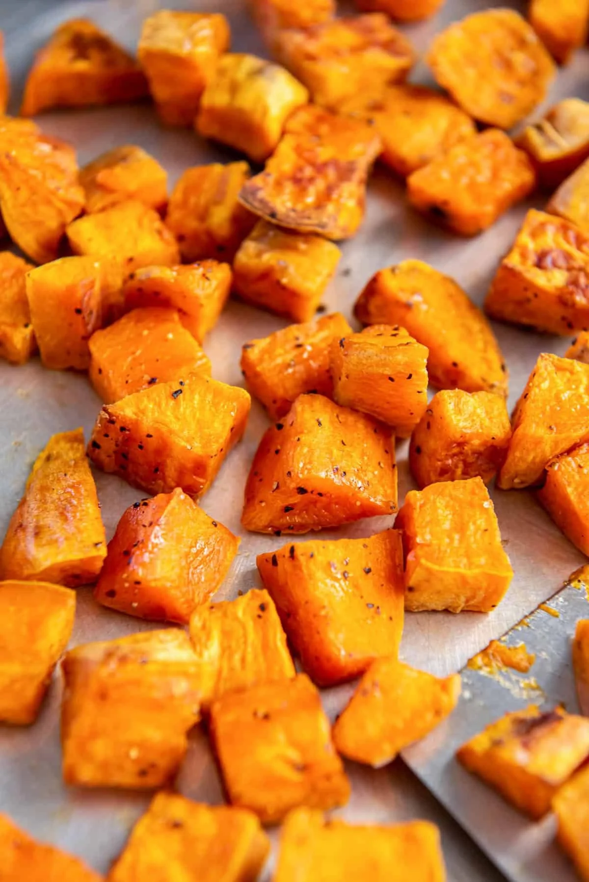 Close-up of roasted sweet potato cubes on a baking sheet, golden and caramelized with lightly charred edges.