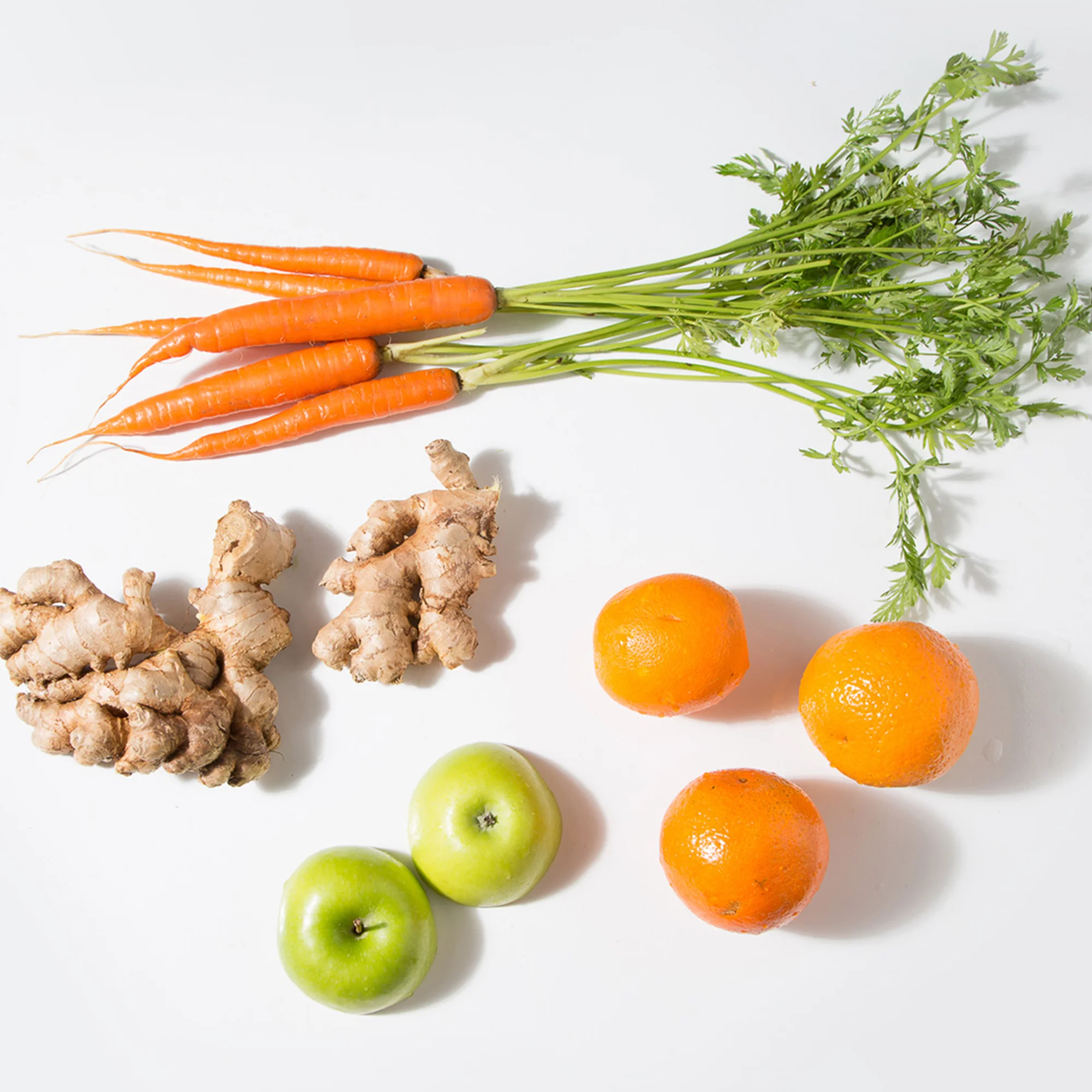 Fresh carrots, ginger, green apples, and oranges arranged on a white background — vibrant whole ingredients perfect for juicing, cooking, or clean-eating recipes. A bright, natural produce flat lay highlighting healthy, raw ingredients.