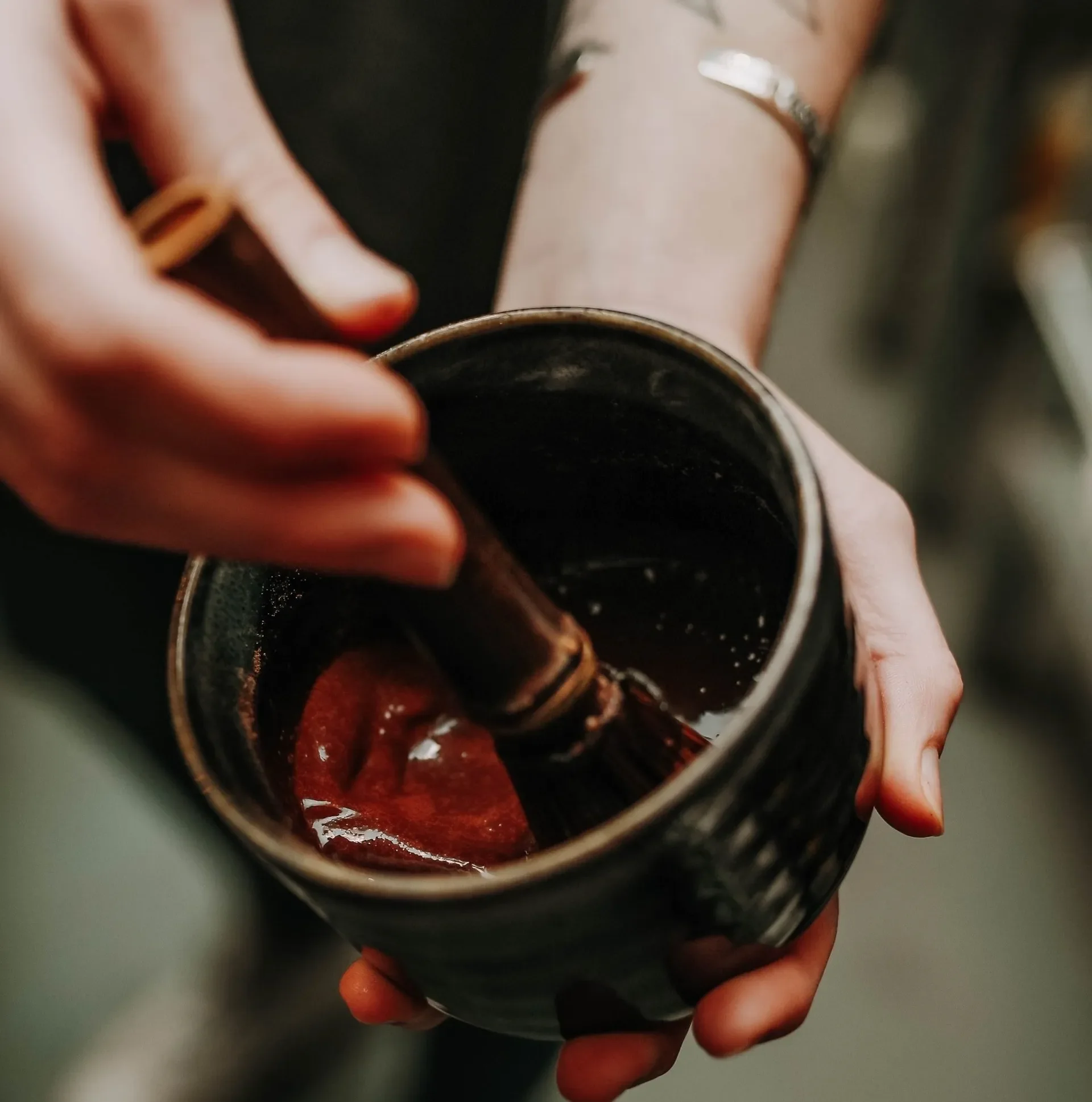 A rich hot chocolate being hand-whisked in a rustic mug using a traditional wooden whisk. Smooth, melted cacao swirls create a cozy, artisan feel, highlighting Raleigh Raw’s warm, crafted hot chocolate experience.