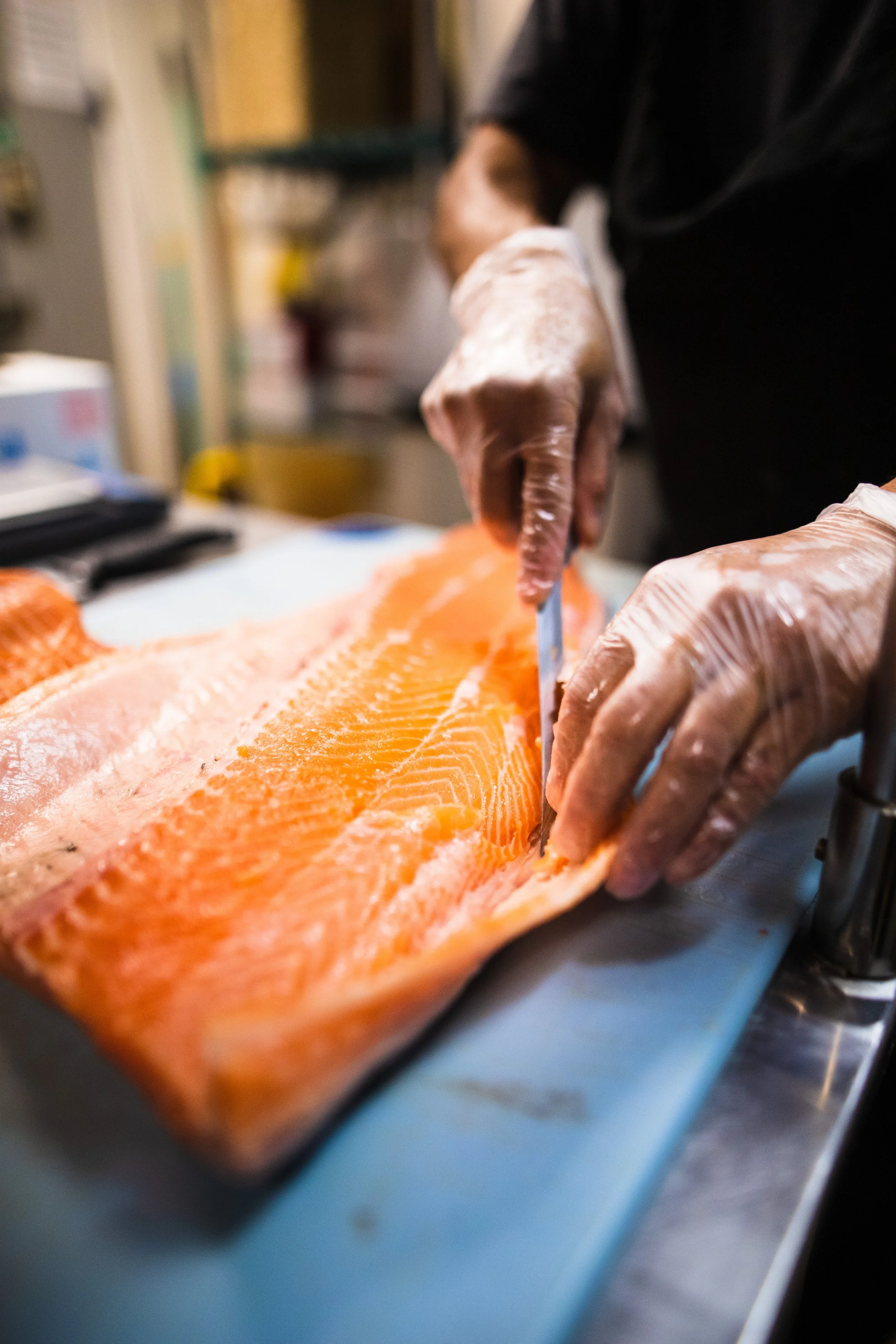 Close-up of a chef in gloves filleting a large, fresh salmon on a cutting board.