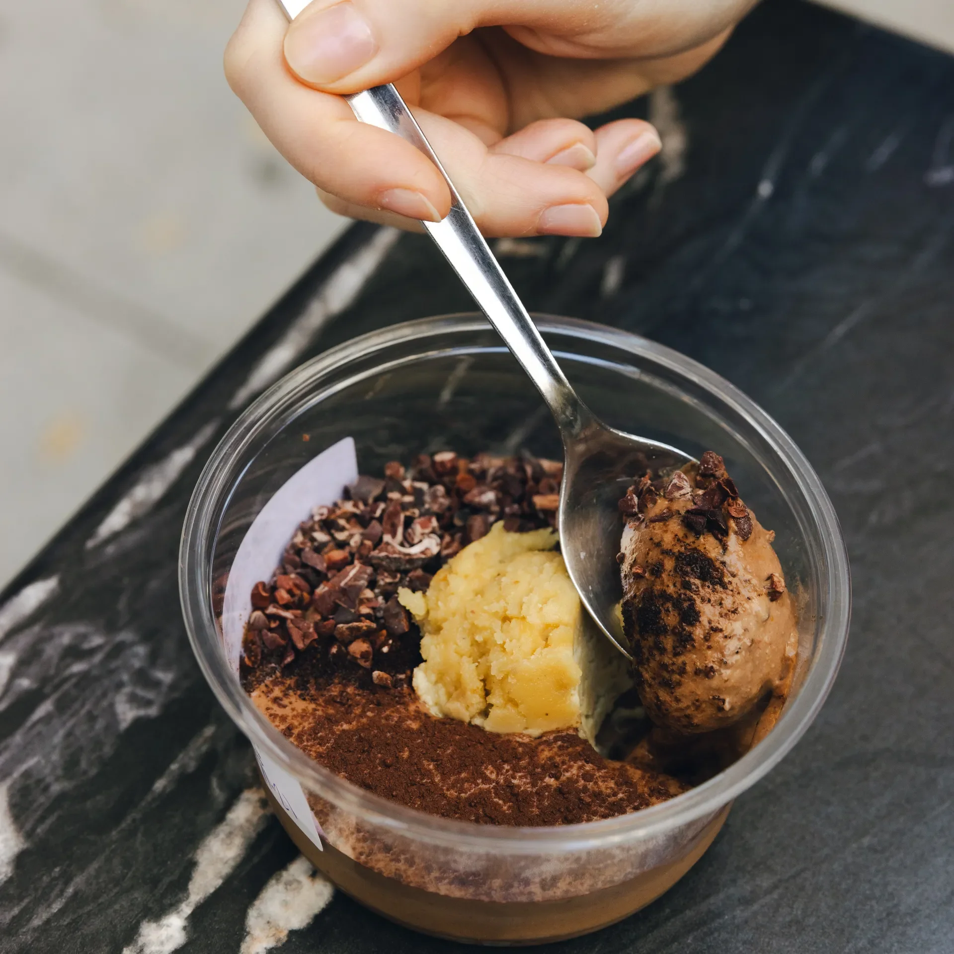 A spoon scoops into Raleigh Raw’s mudpie bowl, layered with cacao, cashew butter, date pudding, and crunchy cacao nibs. A nourishing, gluten-free, soy-free, refined-sugar-free treat crafted for clean energy and whole-food indulgence.
