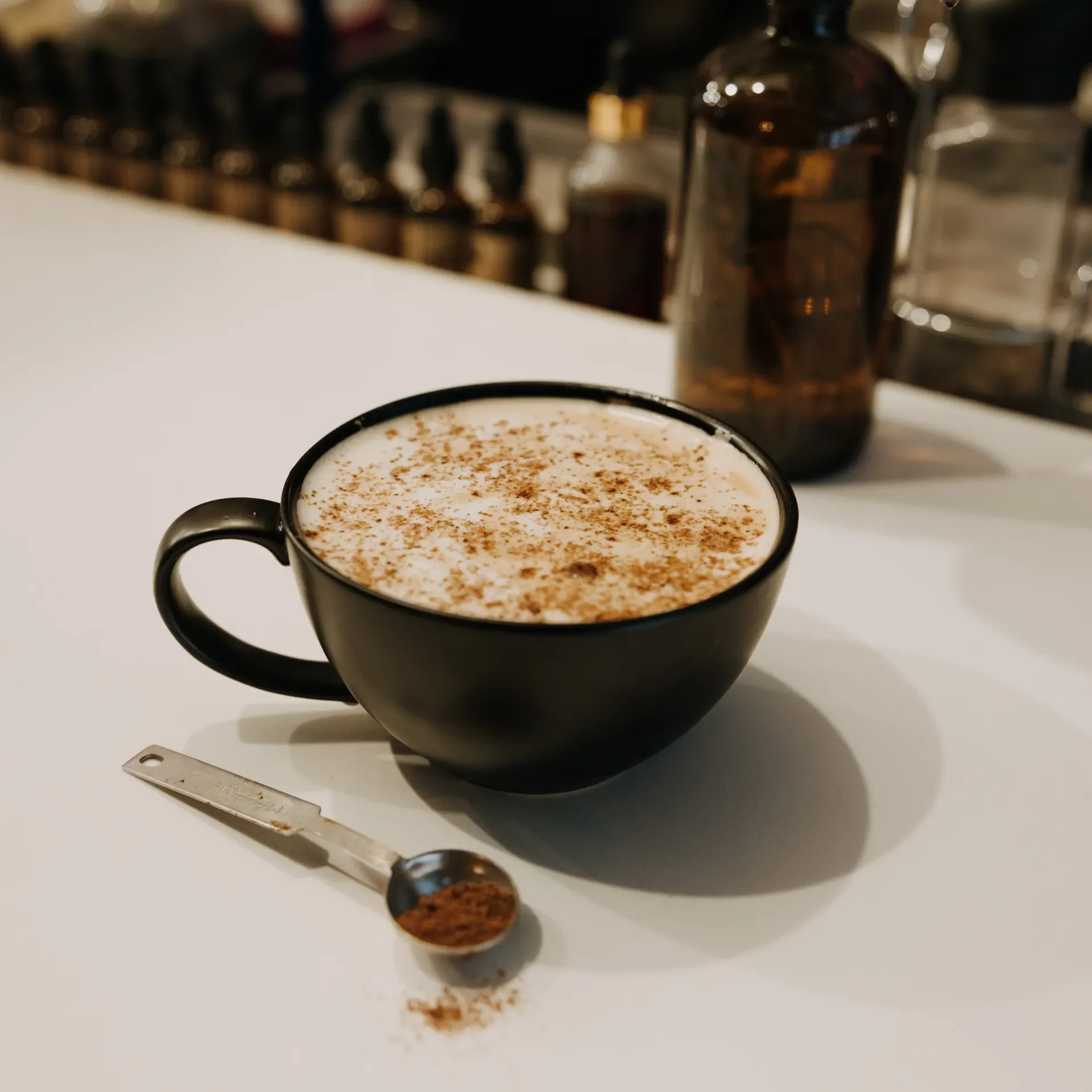 A cozy spiced latte served in a chai black mug at Raleigh Raw, topped with cinnamon for a warm, aromatic finish. A metal teaspoon with spices sits beside it, capturing the café’s handcrafted, intentional beverage experience.