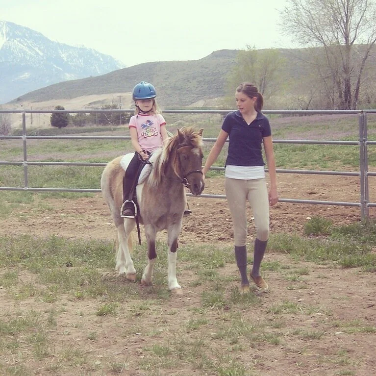 Me at 15 with my first student-my neice Heidi. She’s riding one of my mom’s welsh ponies, Cookie