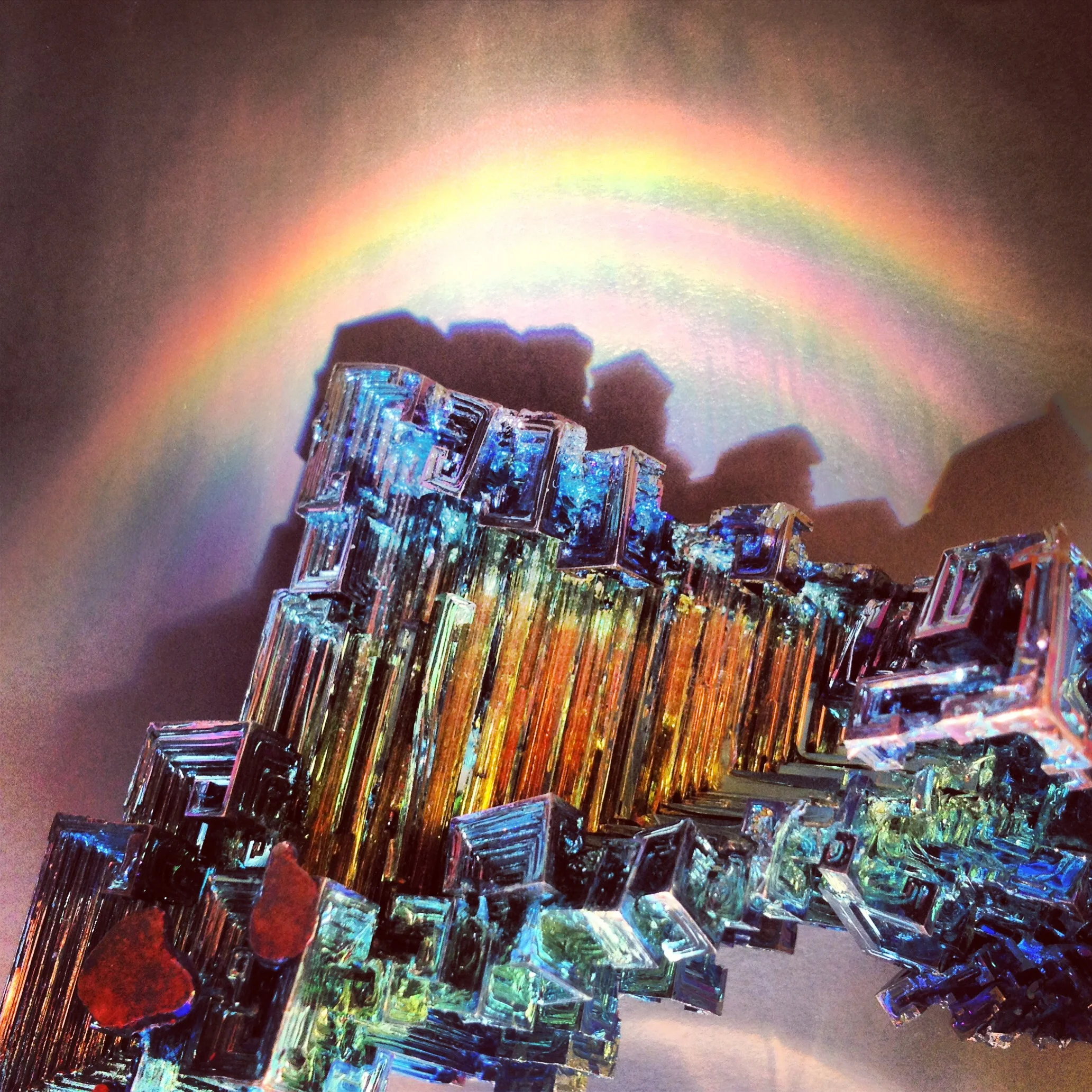 Bismuth is a brittle metal with a white silver pink yellow blue hue and iridescent oxide tarnish. The spiral stair shaped structure is the result of higher growth rate around the outside edges than the inside edges. Iridescent: meaning rainbow, which in turn derives from the goddess Iris of Greek mythology.