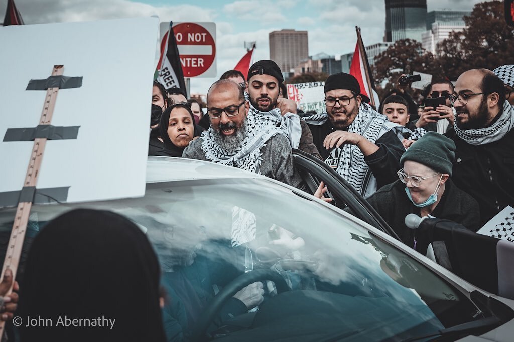 Apparently this man said &ldquo;fuck Palestine&rdquo; out his car window at this Palestine protest. He was getting out of his car with a knife in his hand. You can see it in this photo. The woman in the green hat is spaying mace on him. She can be cr