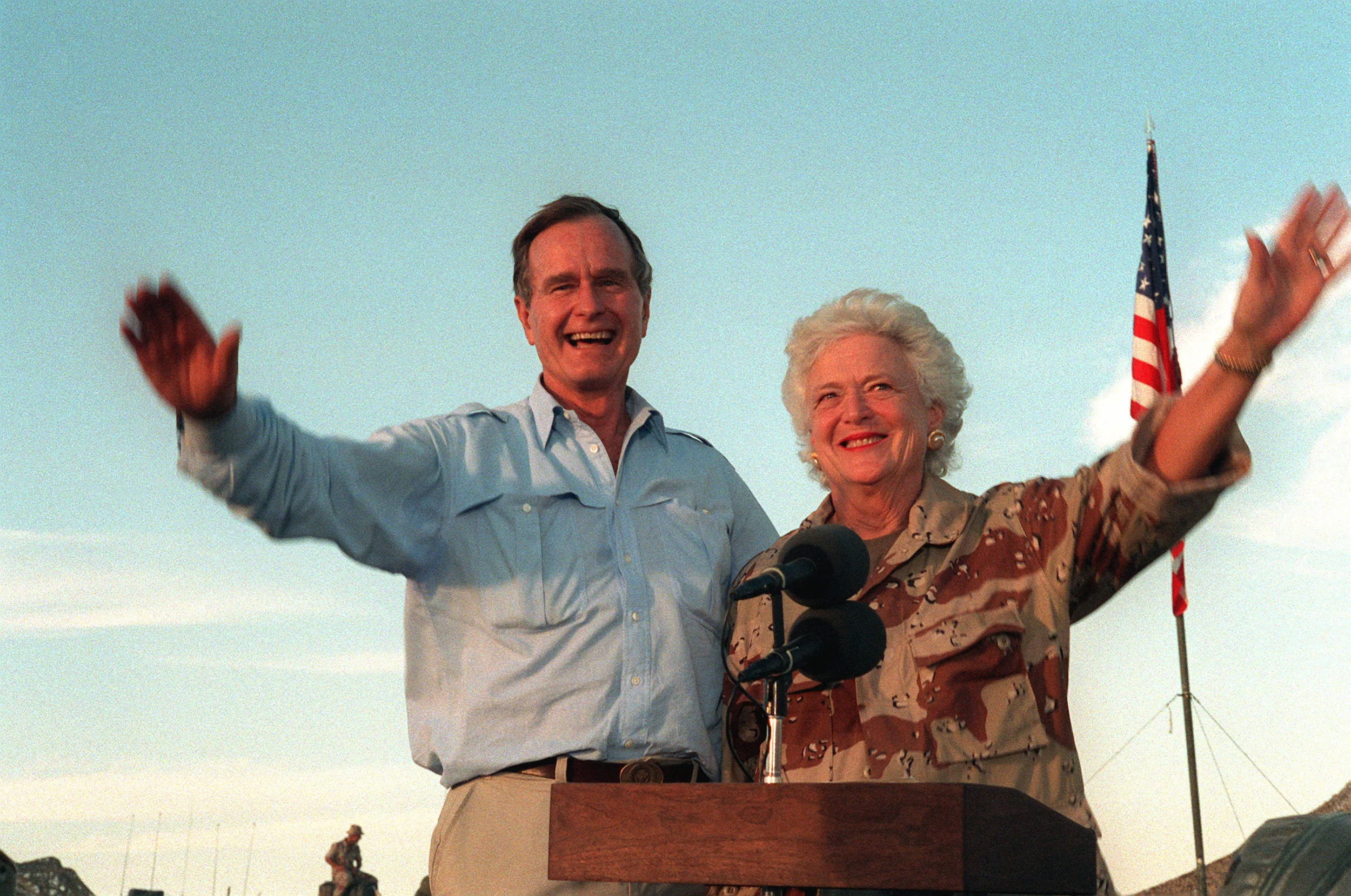 U.S. President George H.W. Bush and first lady Barbara Bush wave as they stand in the back of a vehicle during a visit to a desert encampment in Saudi Arabia, Nov. 22, 1990. The president and his wife are paying Thanksgiving Day visits to U.S. troops who are in Saudi Arabia for Operation Desert Shield. (U.S. Navy photo by CW02 Ed Bailey)