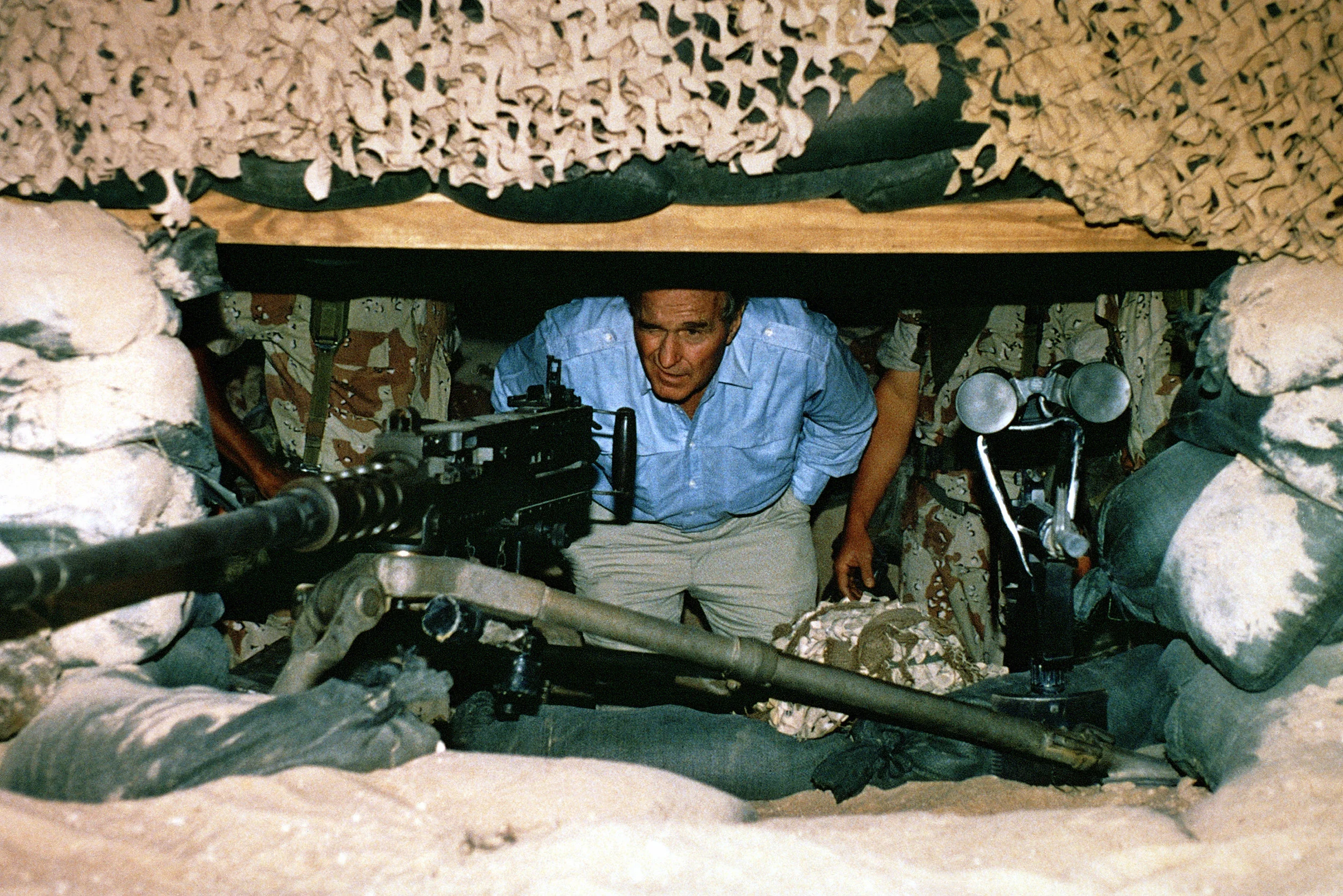 President George H.W. Bush peers out from a bunker at an M2 .50-caliber machine gun on Nov. 22, 1990. The president is in Saudi Arabia during the Thanksgiving holiday to visit U.S. troops deployed to the area during Operation Desert Shield. (Photo by Capt. Michael Edrington)