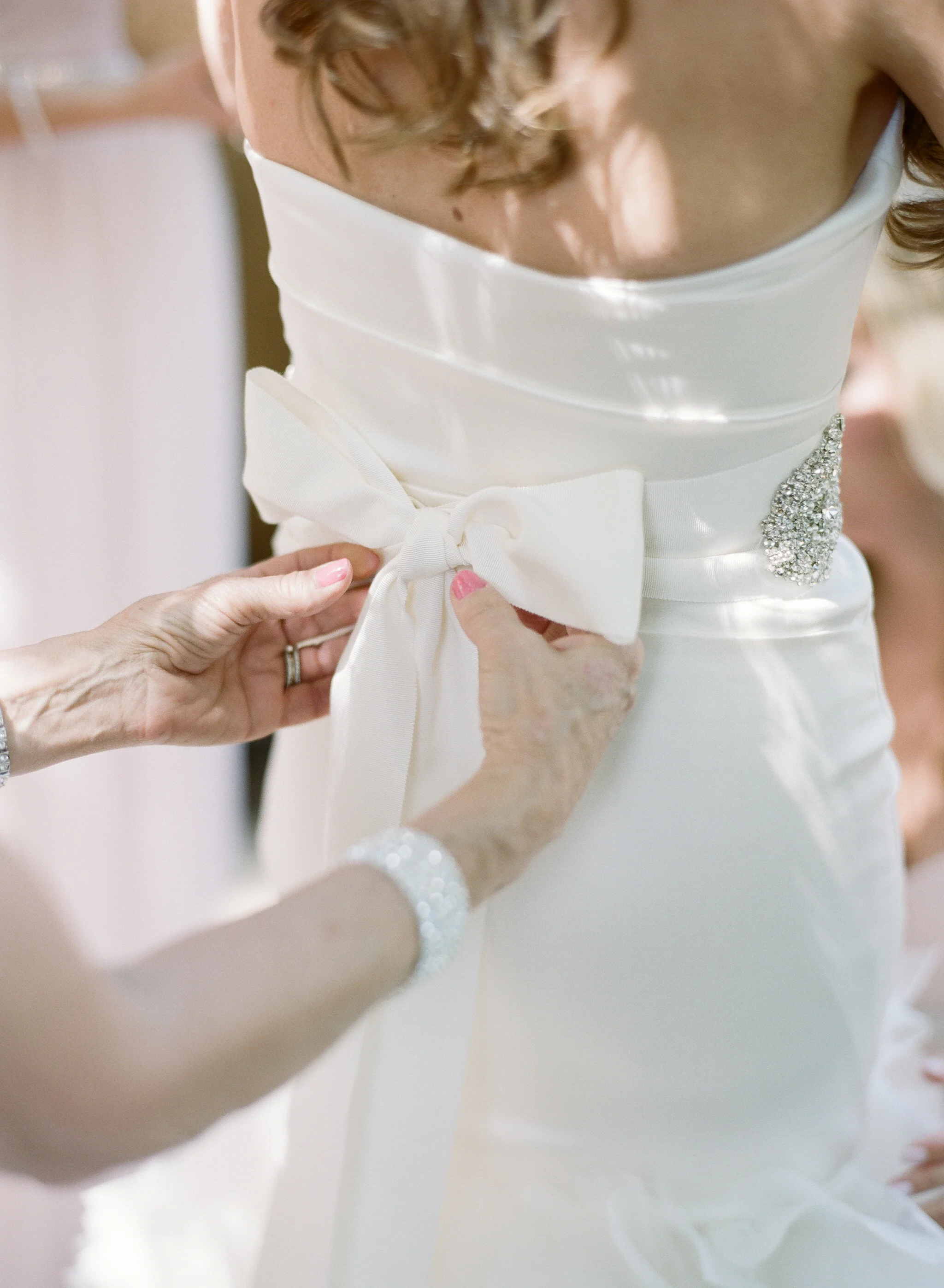 A member of the bridal party ties the gown on the back of Lauren's elegant strapless wedding gown; photo by Sylvie Gil