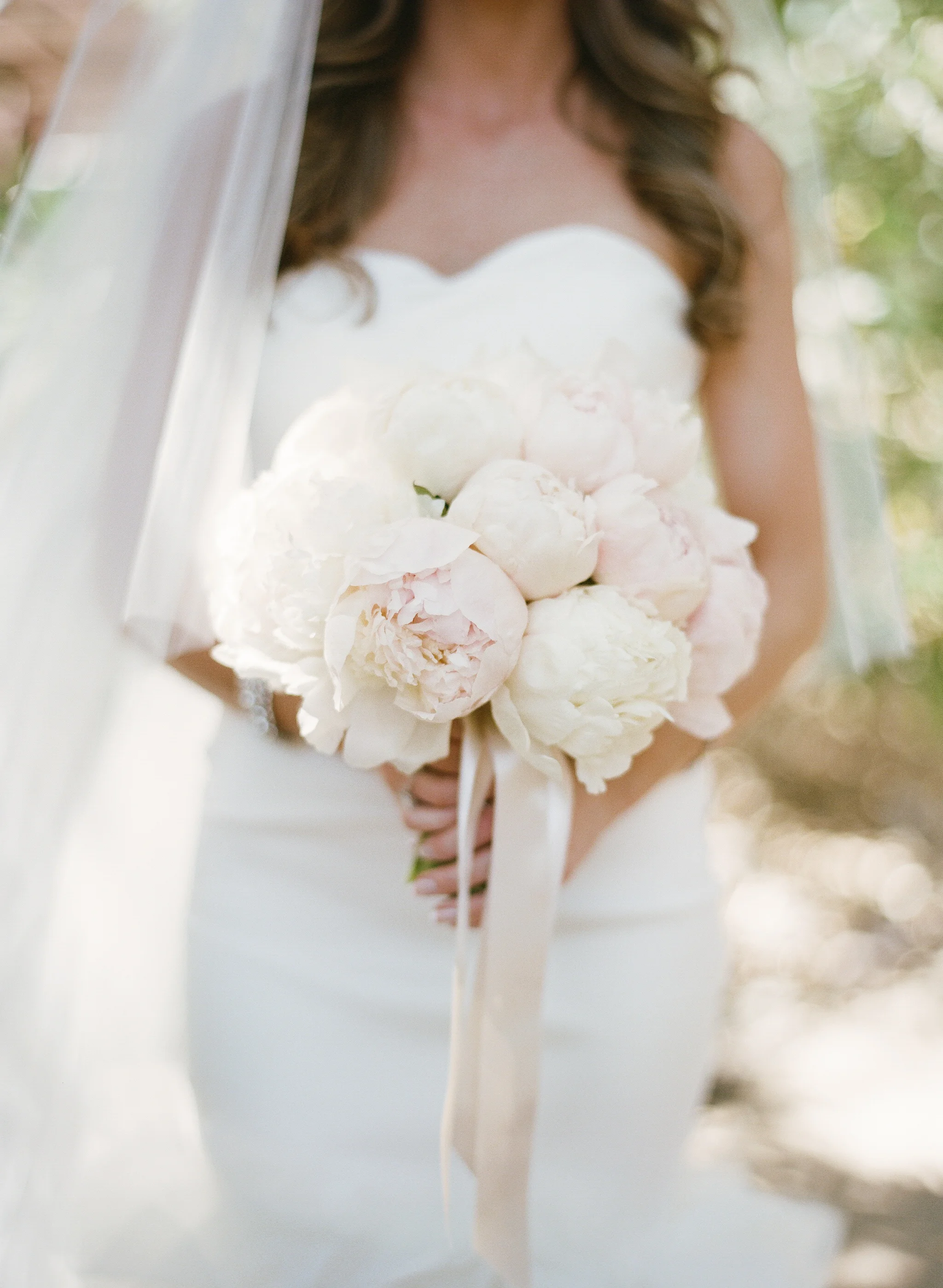 A glowing bride holds her bouquet of white and blush florals, wearing a strapless sweetheart-neckline gown; photo by Sylvie Gil