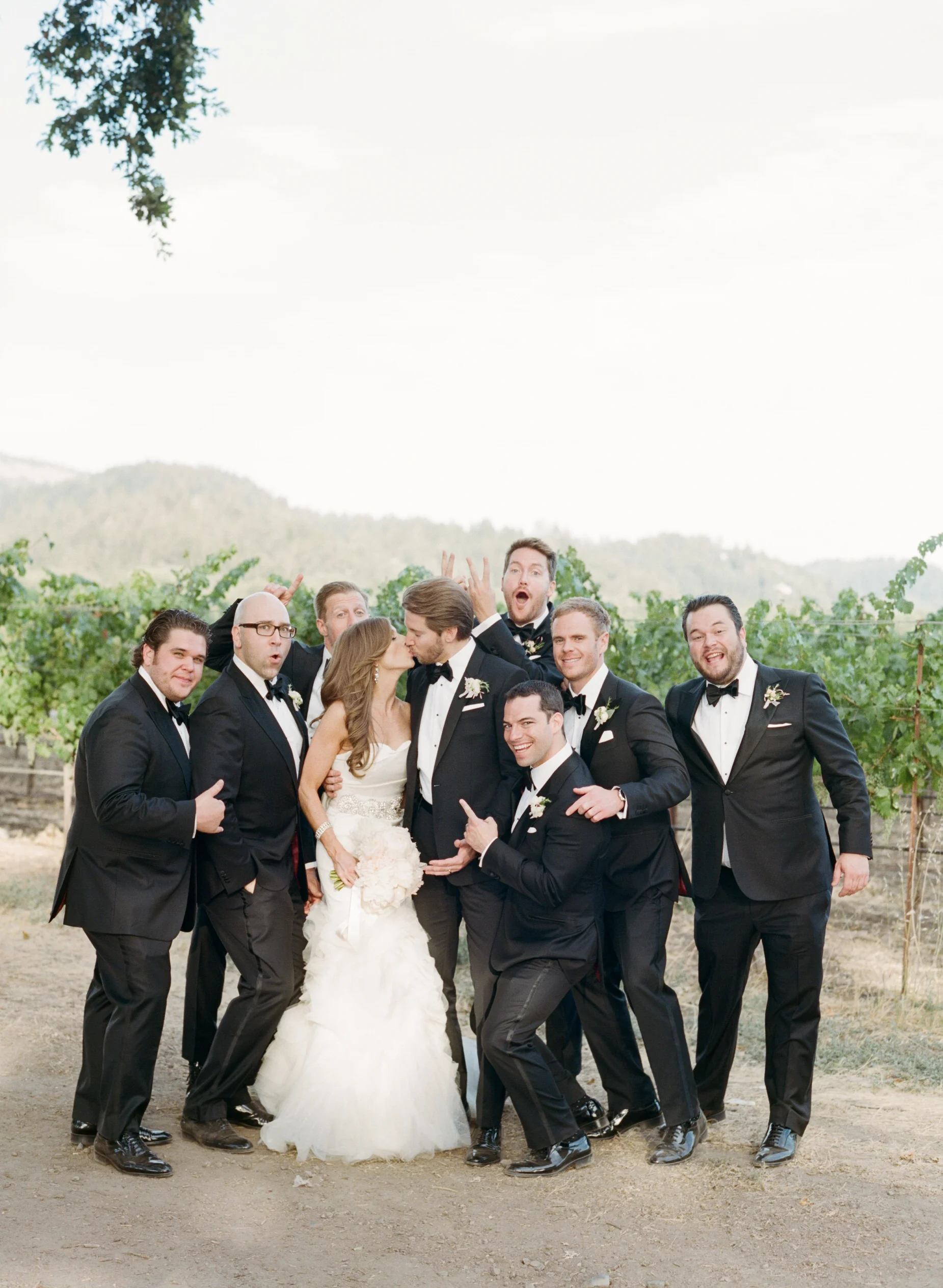 Michael kisses his bride, surrounded by his goofy groomsmen, posing for a silly shot; photo by Sylvie Gil