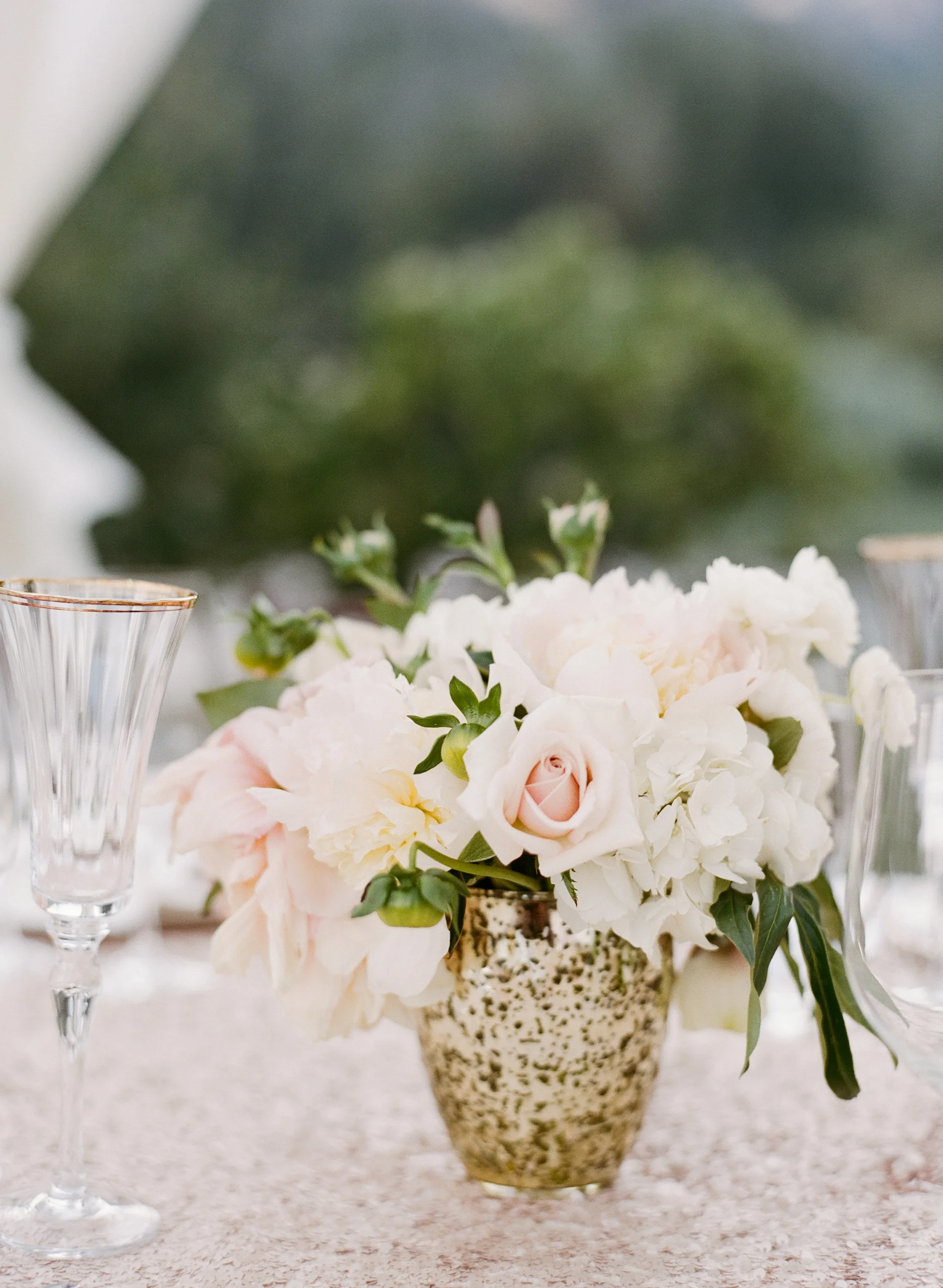 A gorgeous blush centerpiece arranged in a gilt vase decorates the outdoor reception table; photo by Sylvie Gil