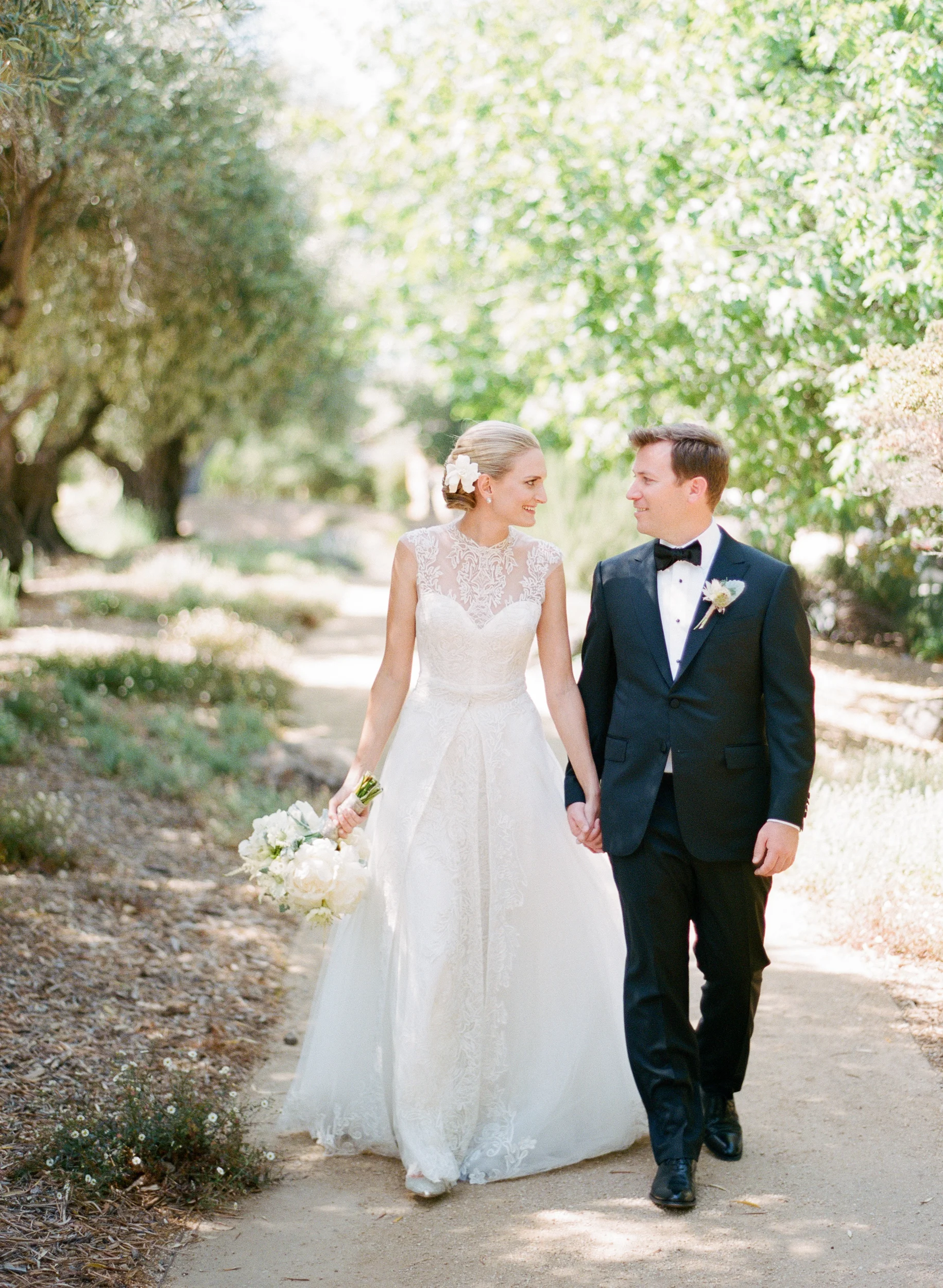 Bride and groom walk holding hands through olive trees in Calistoga Ranch; Sylvie Gil Photography