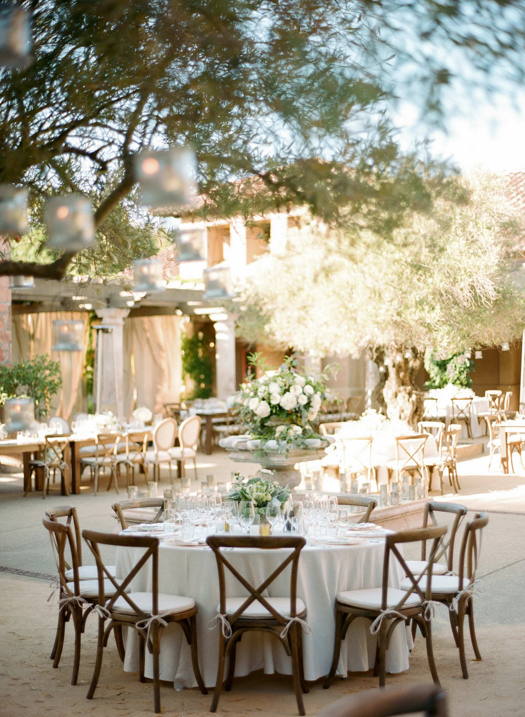 Outdoor reception tables arranged in Calistoga Ranch courtyard under olive trees; Sylvie Gil Photography