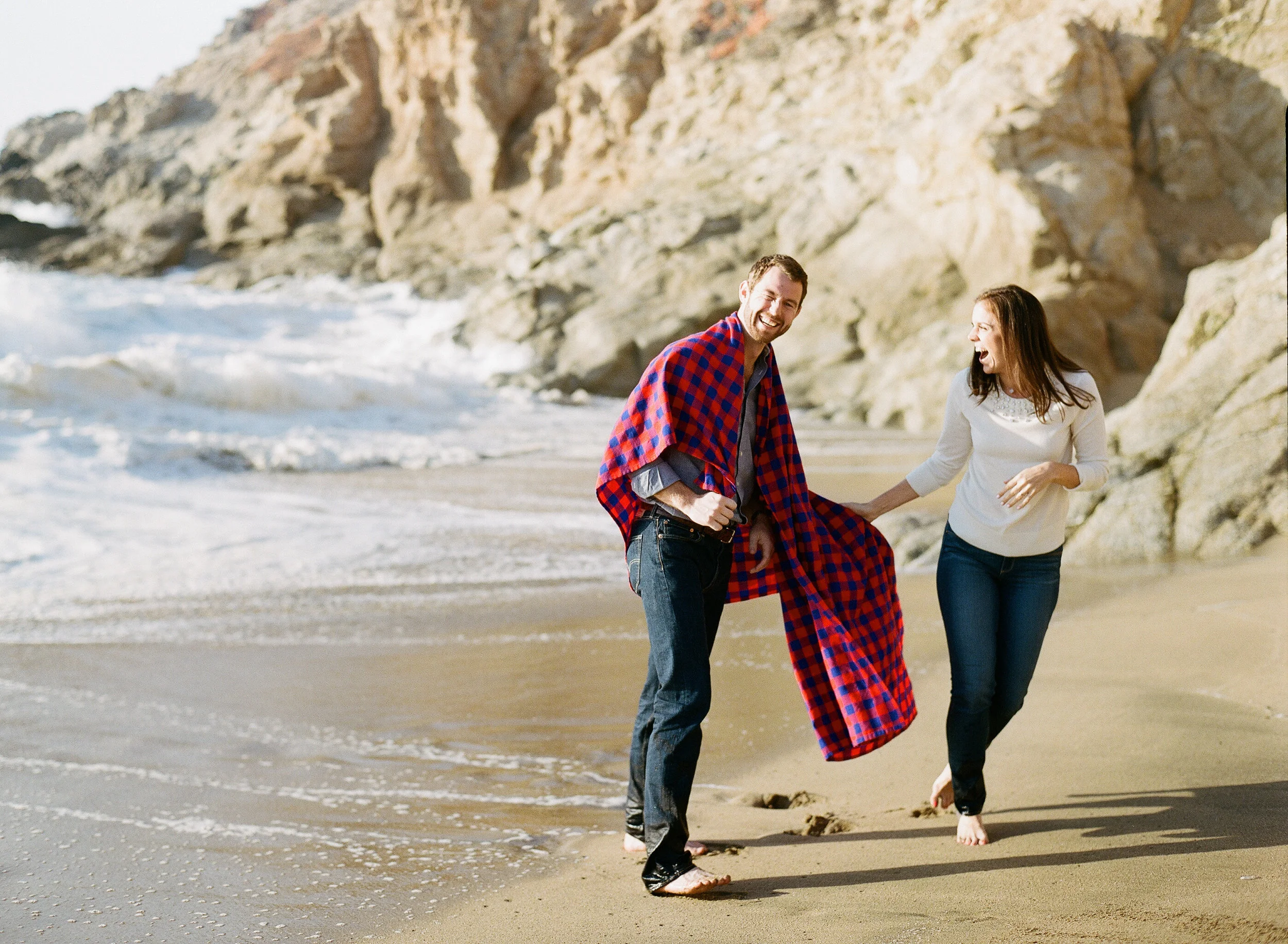 Couple plays on the beach during engagement session photo shoot; Sylvie Gil Photography