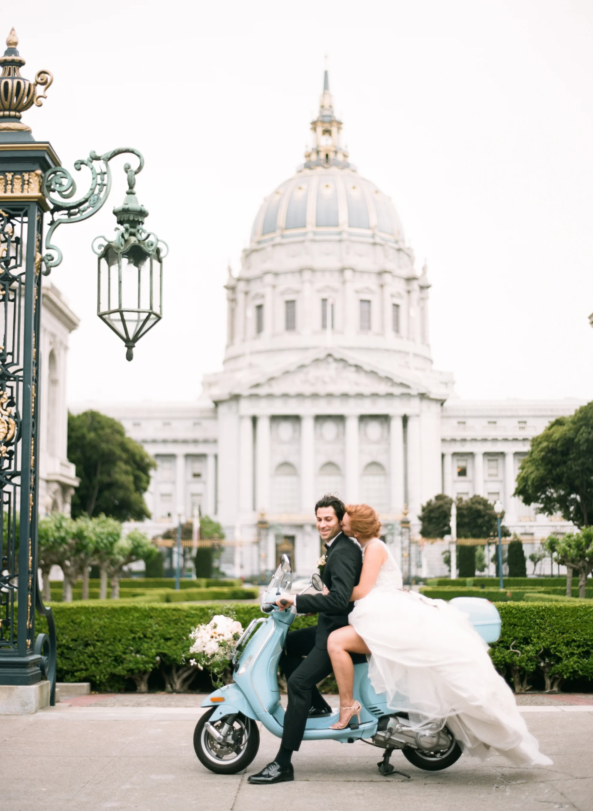Bride and groom sit on a turquoise Vespa scooter outside San Francisco City Hall; Sylvie Gil Photography