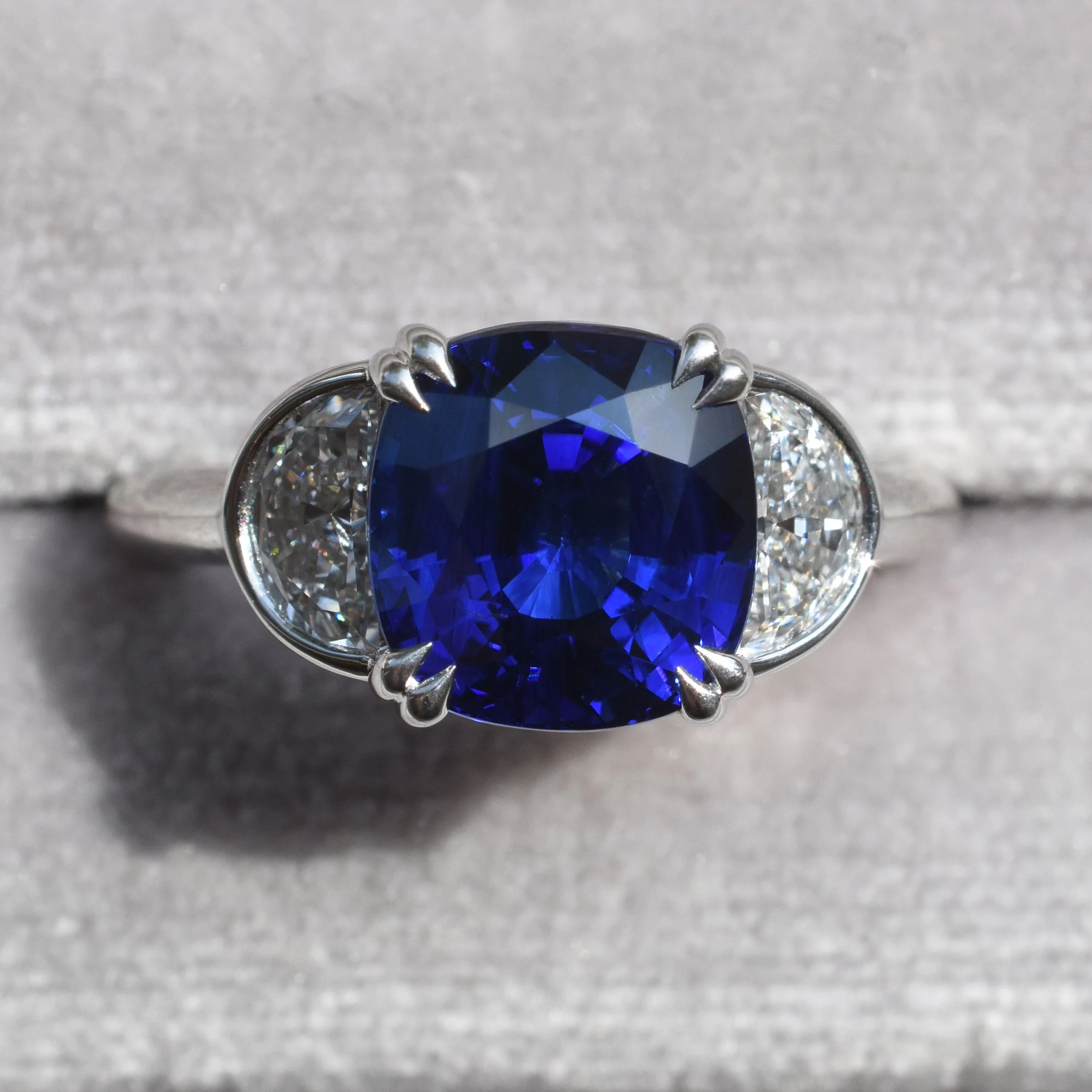 Ring with a large, oval-shaped deep blue natural sapphire flanked by smaller lab grown diamonds on each side, set in a platinum band.
