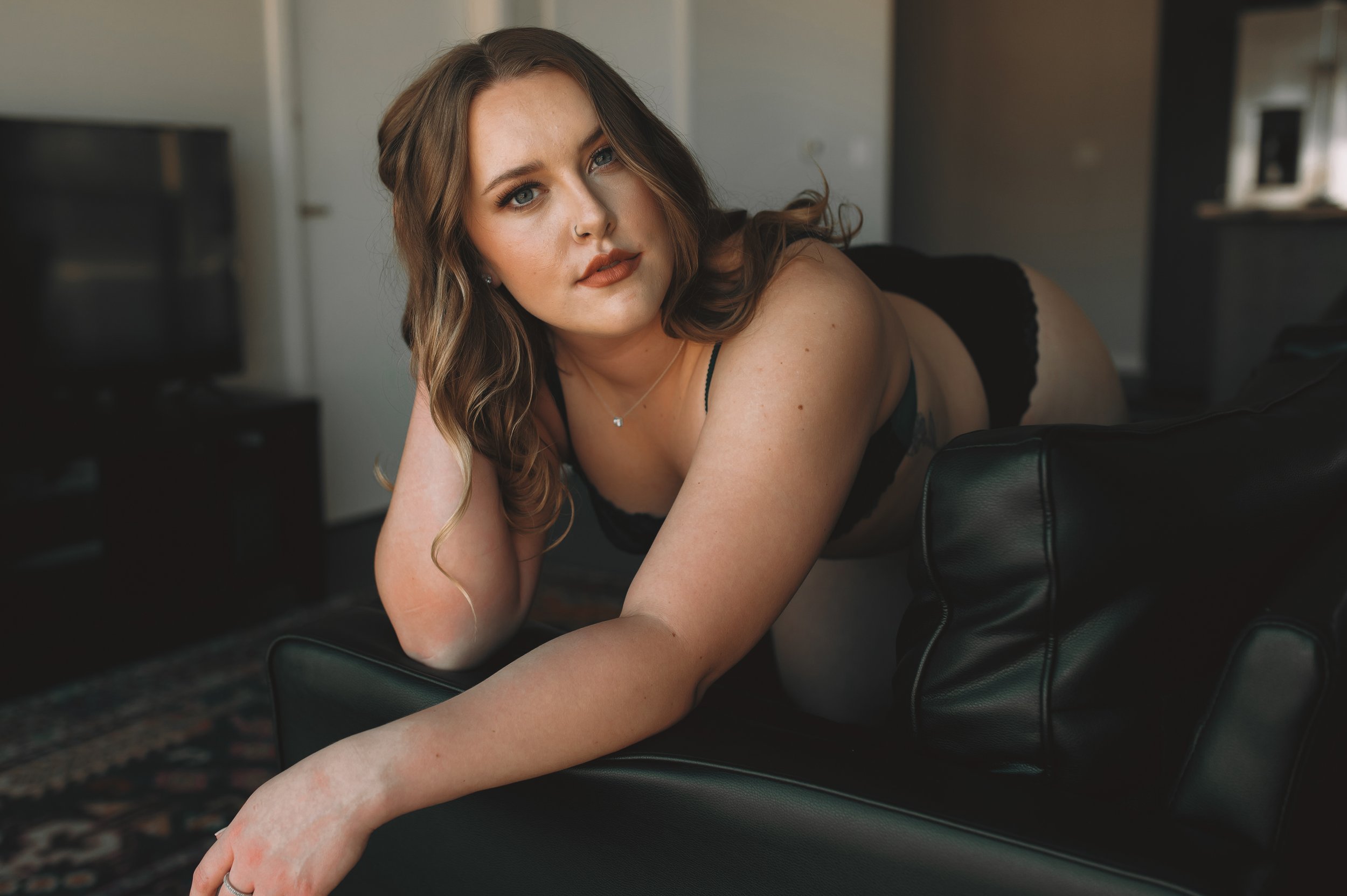 Blonde woman kneels on black leather sofa in sleek apartment