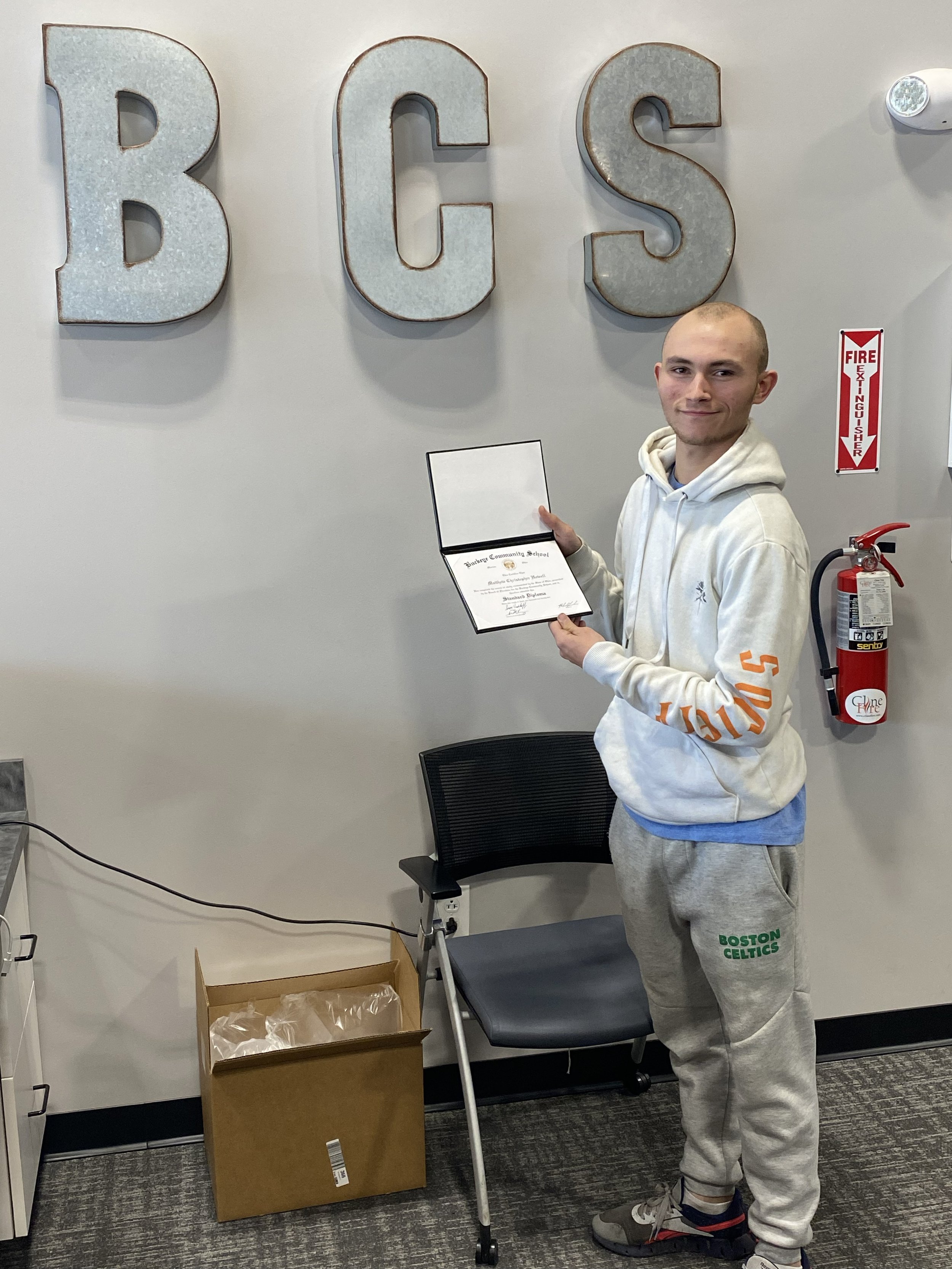 Person holding a certificate in front of wall with large letters "BCS."