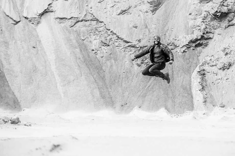 A man jumps in the air with a big smile in a rocky canyon with sandy ground.