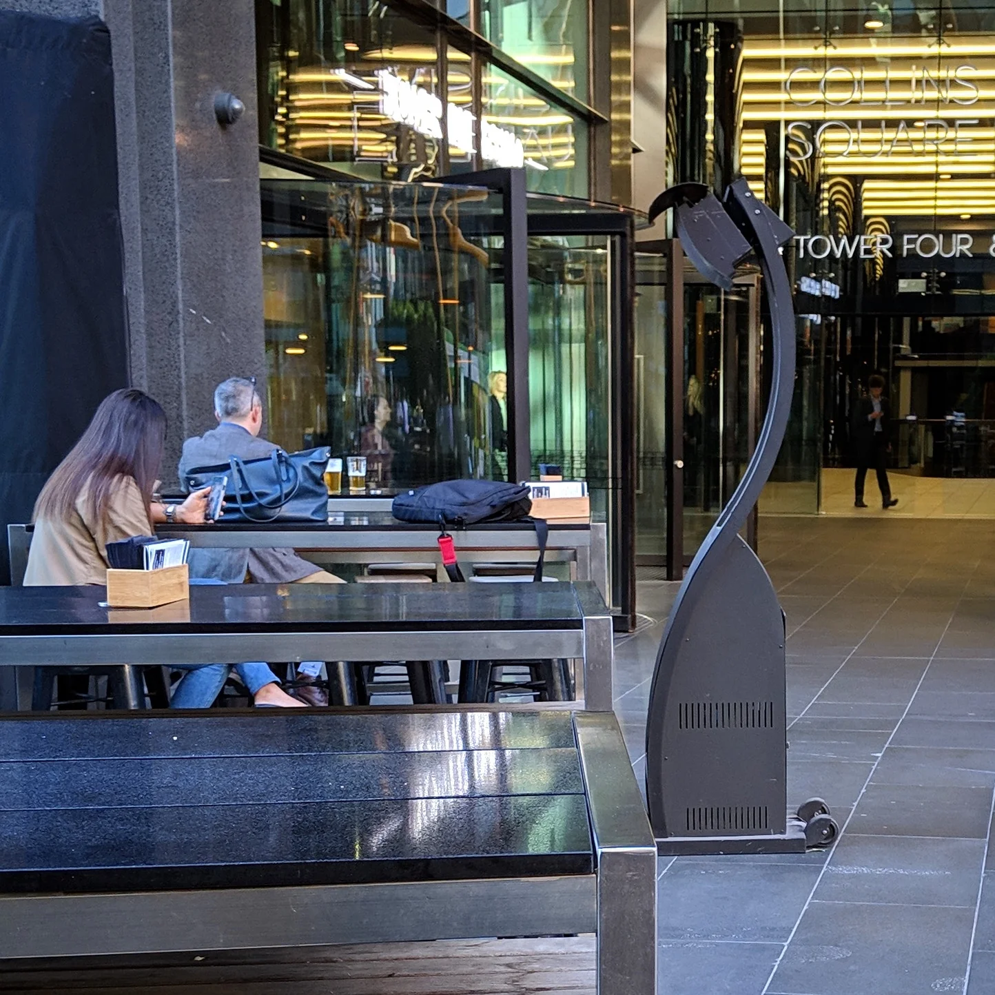 A large outdoor space heater warms people who are sitting at an outdoor table of a cafe in Docklands, Melbourne.