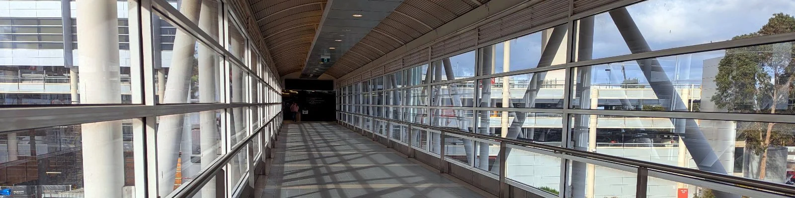 Wide-angle photo of an elevated, covered walkway leading to Melbourne Airport Teminal 2 from the main, mult-level car park..