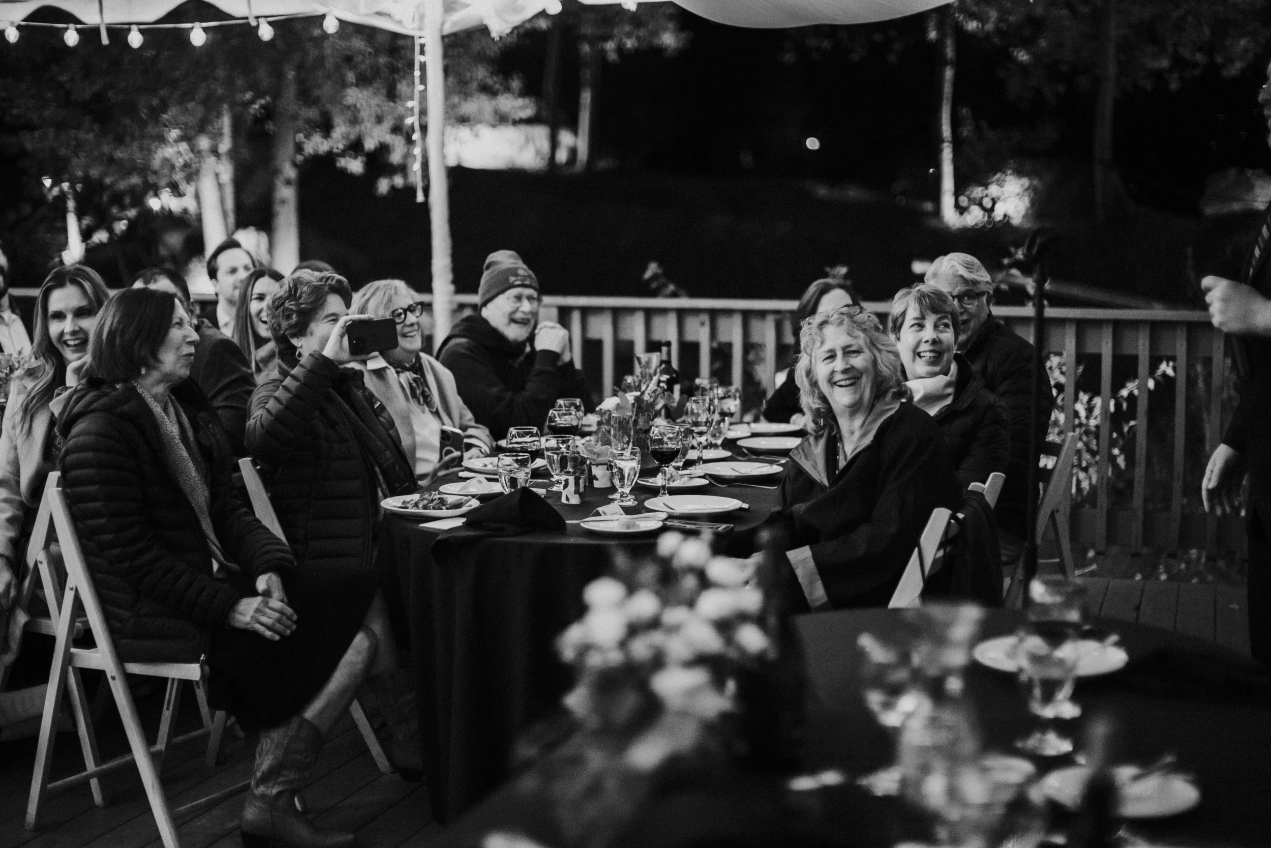 People gathered around a table at an outdoor wedding reception, smiling and enjoying each other's company, with some taking photos at a beautiful resort in California by Dorey Kronick