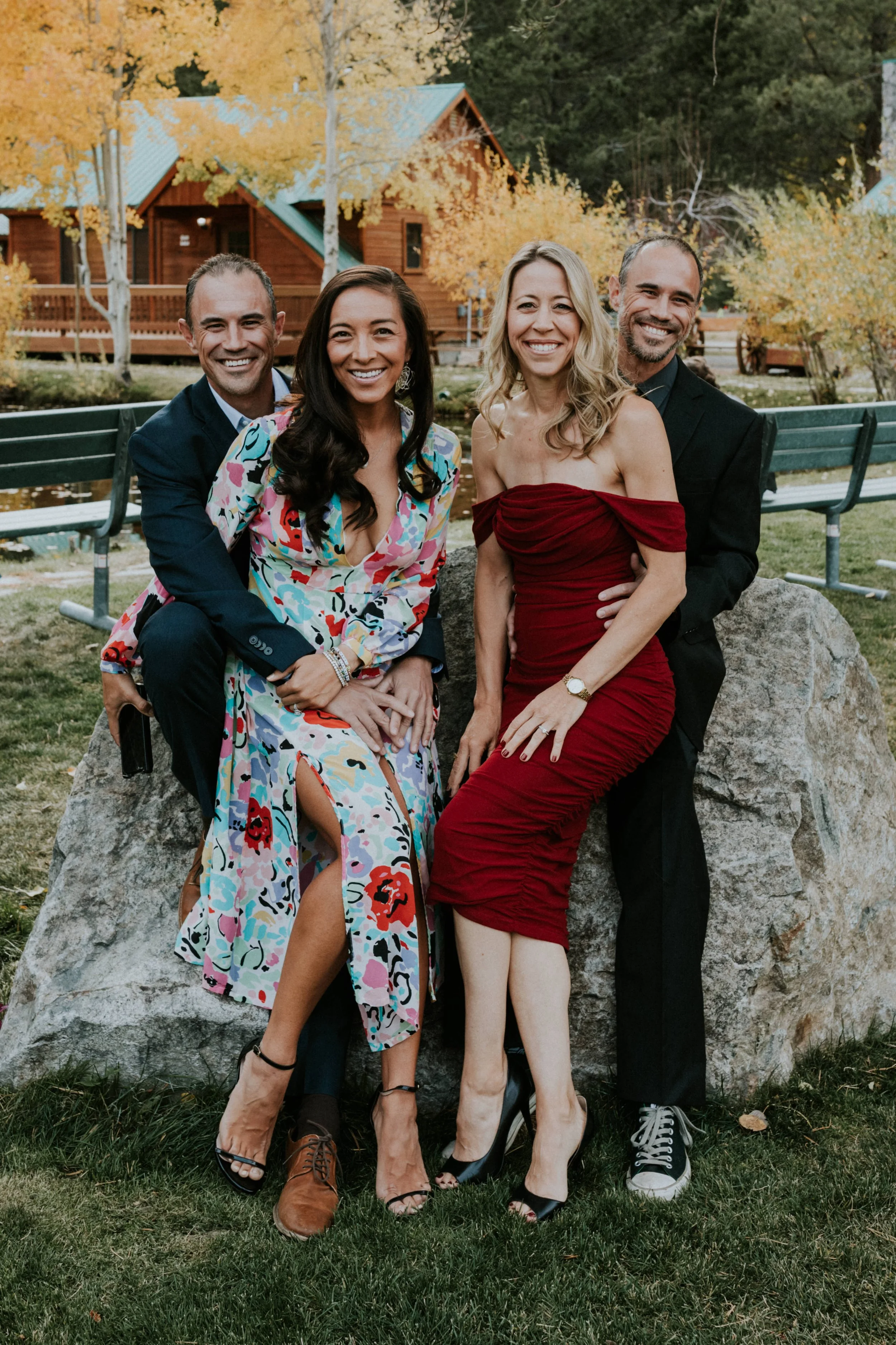Four nicely dressed people at a wedding in Mammoth, CA, posing outdoors near a lake and wooden cabins, during autumn by Dorey Kronick