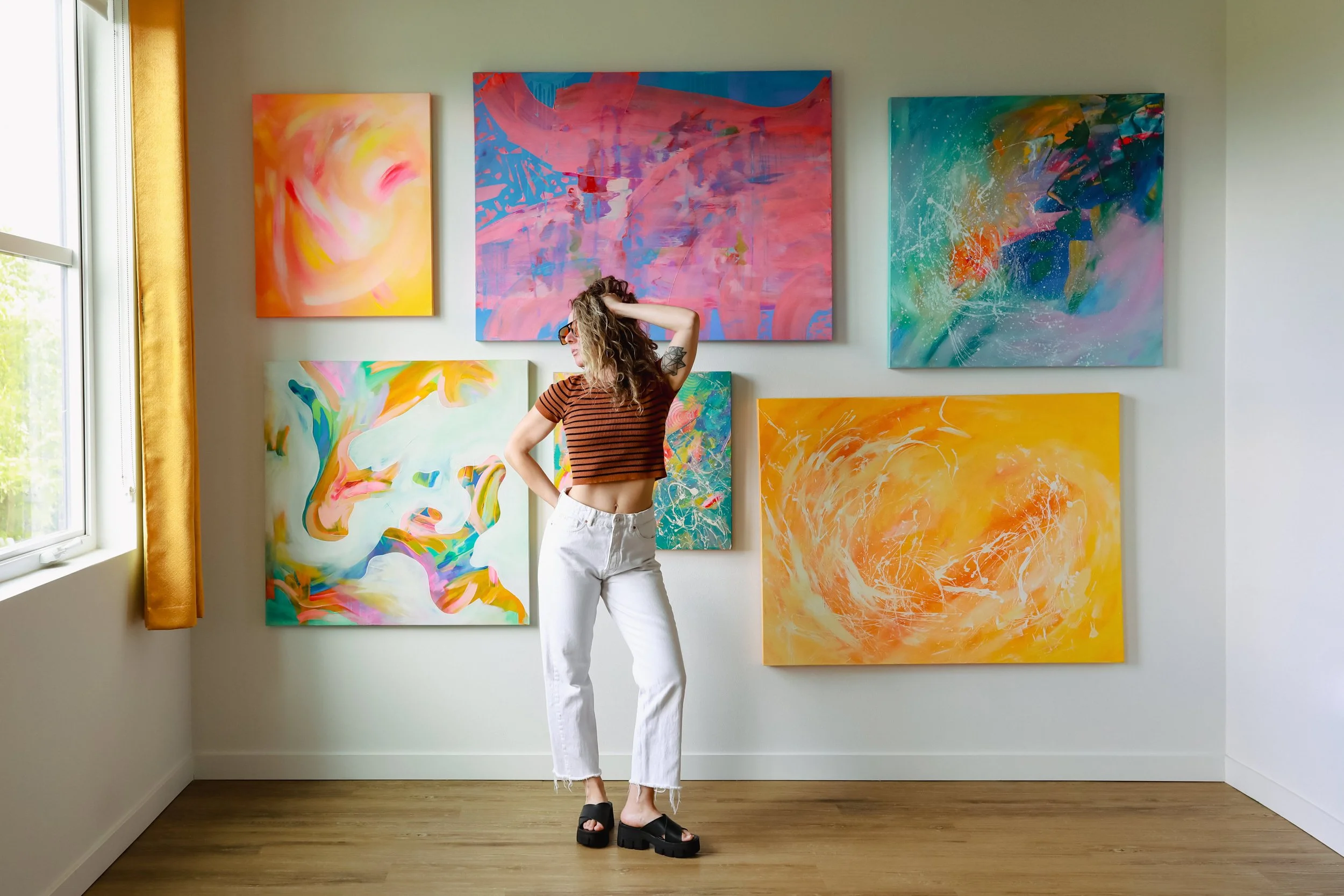 Portland Artist, Dorey Kronick, standing in front of her expressionist painting series titled, "Merging the Sides of Myself" in her Mississippi Neighborhood studio in 2024