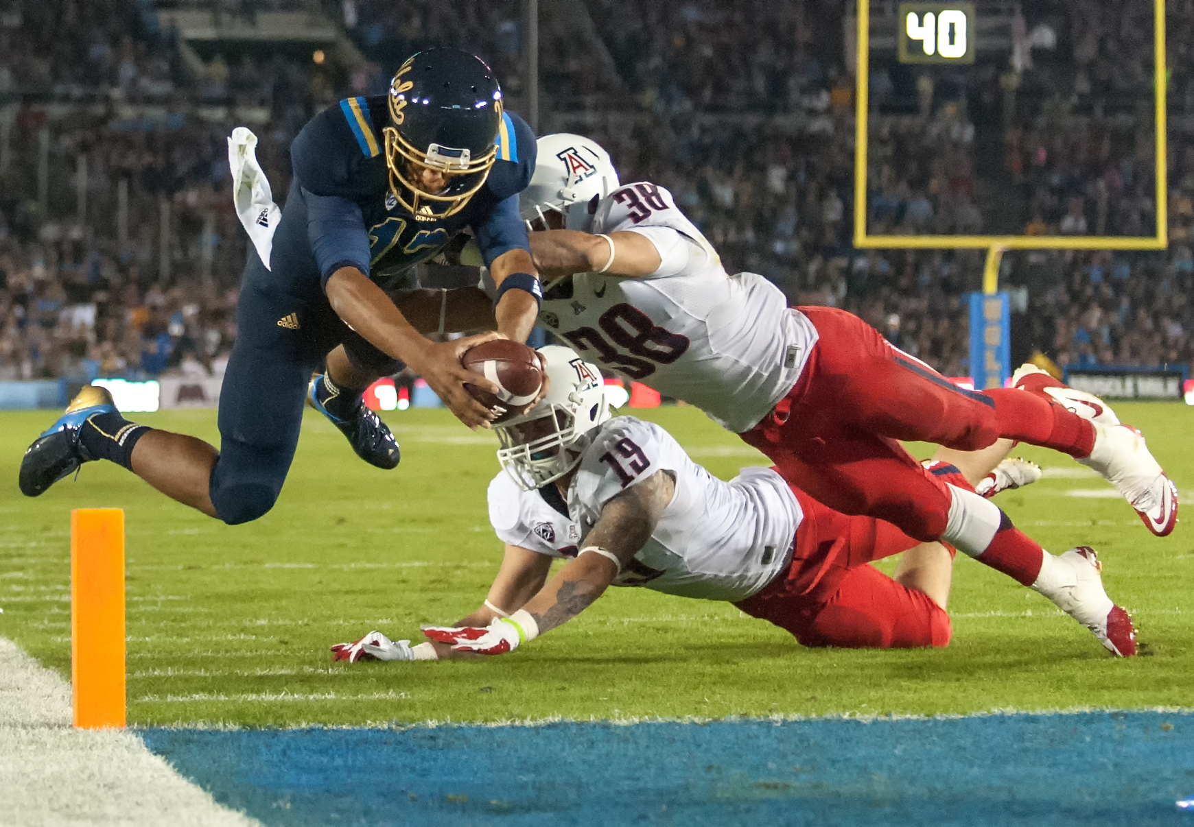  ​PASADENA, CA – Redshirt freshman quarterback Brett Hundley dives toward the endzone past Arizona sophomore linebacker Hank Hobson (center) and sophomore safety Jared Tevis at the Rose Bowl on Saturday, November 3, 2012. 