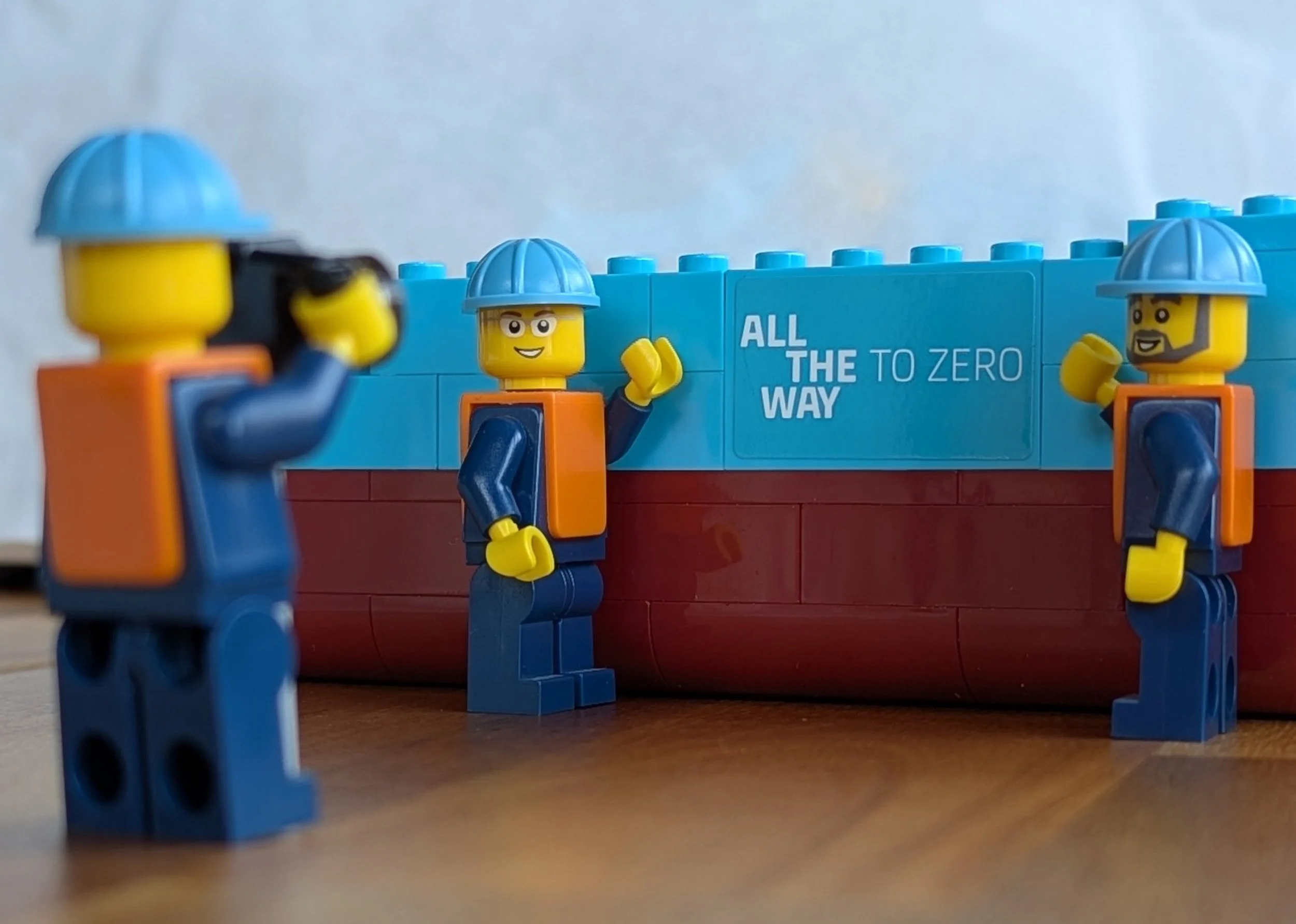 Minifigure construction workers posing with the "All the way to zero" sign.